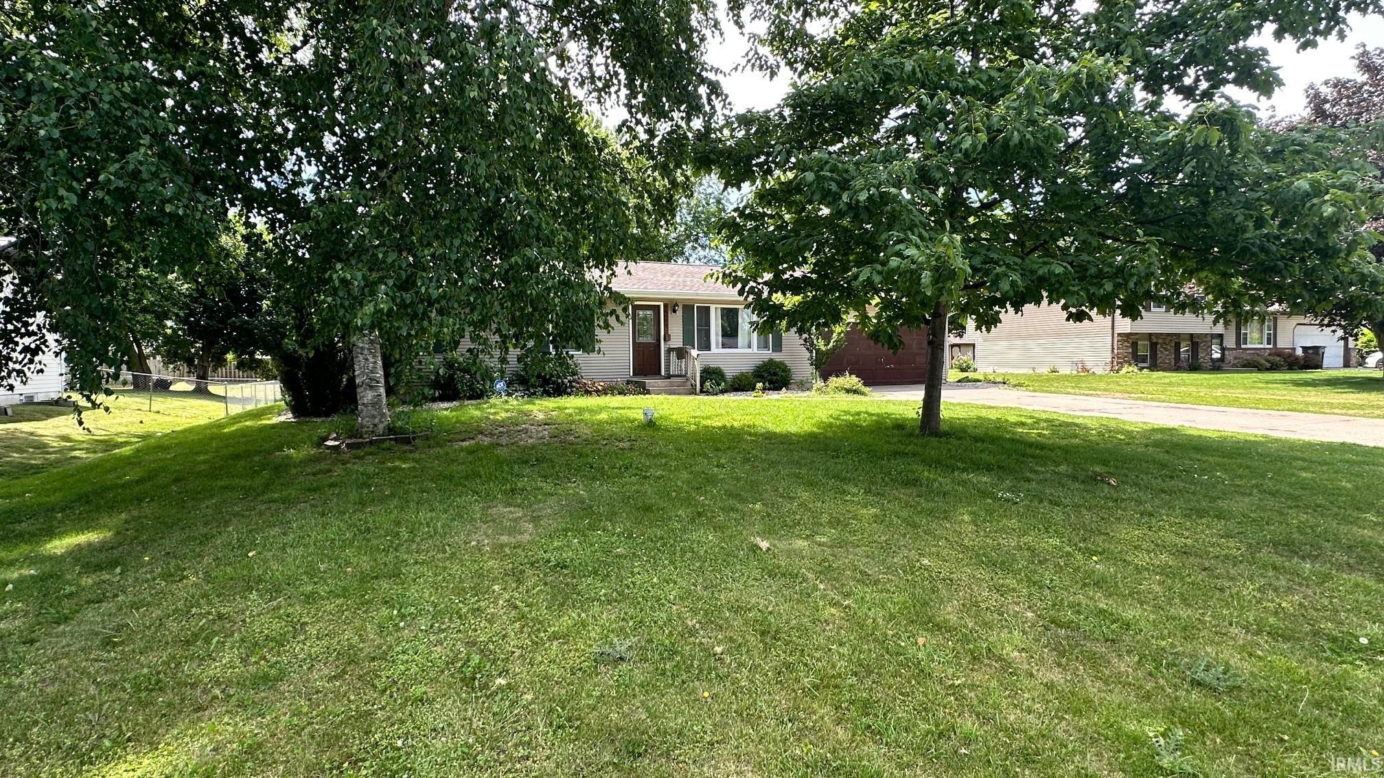 Ranch-style residence featuring a prominent front lawn with mature trees and a paved driveway