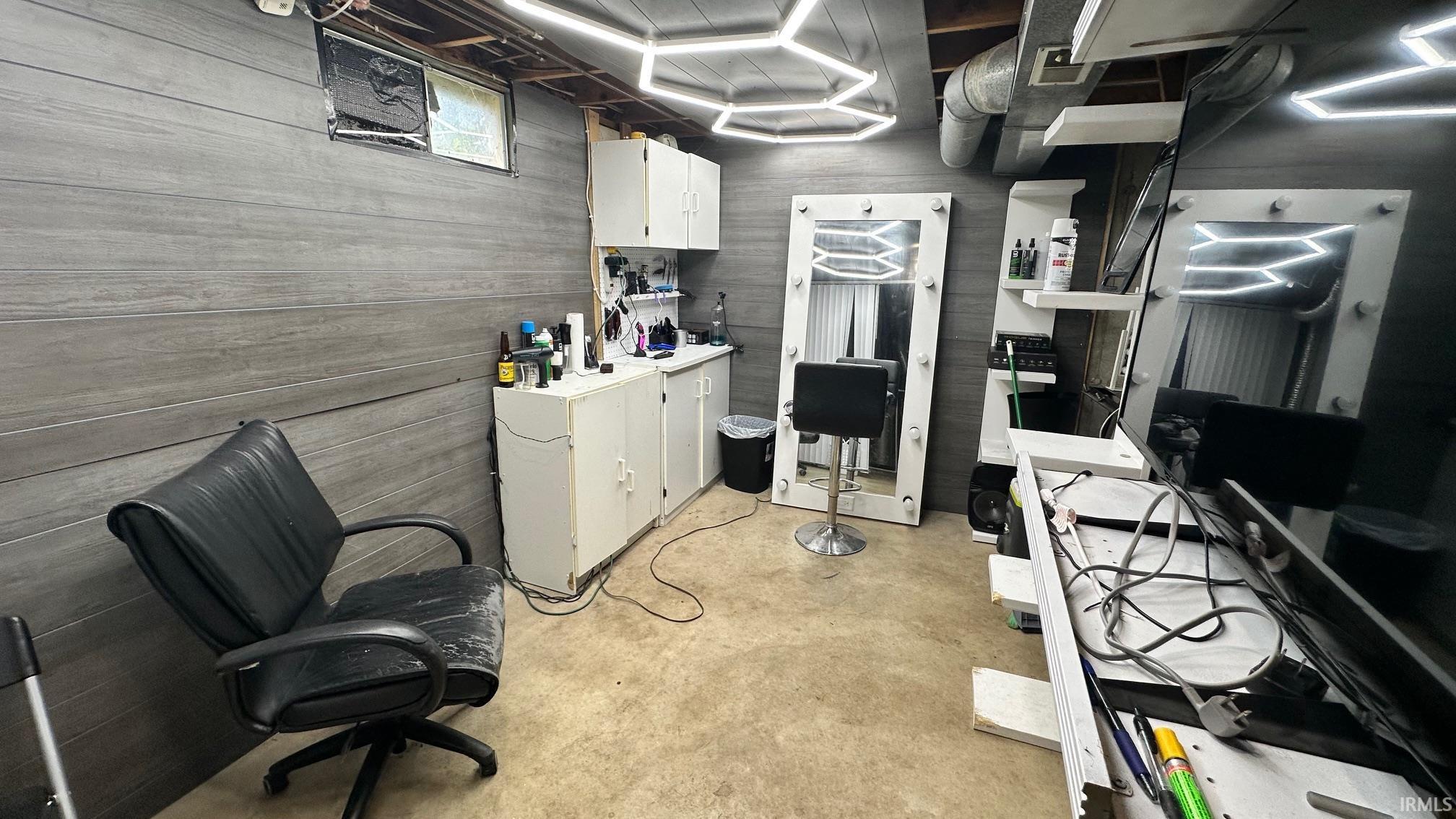 Finished basement space featuring horizontal gray wall paneling, multiple illuminated hexagonal light fixtures, and white base cabinetry with shelving