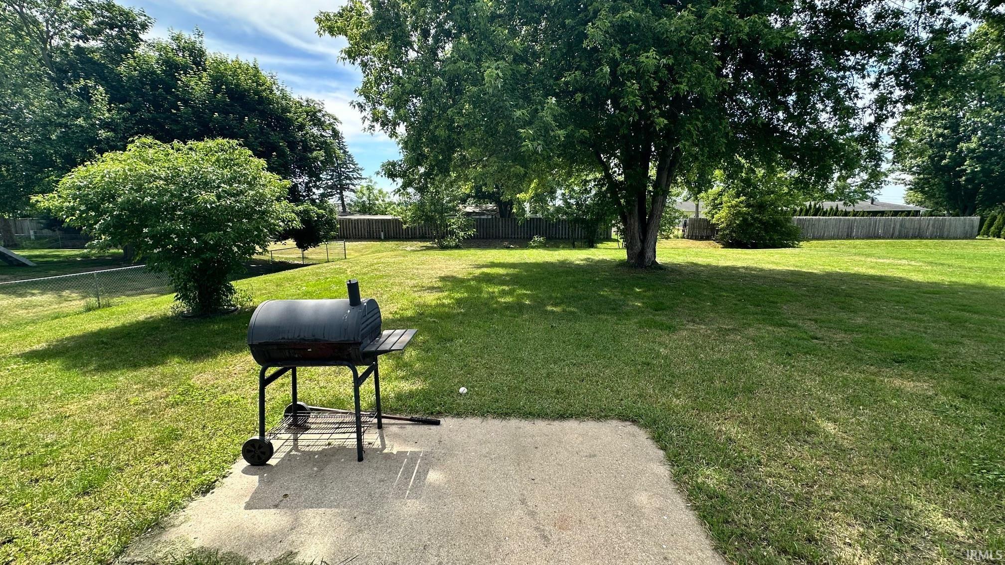 Expansive backyard featuring a concrete patio, mature trees, and a wooden privacy fence