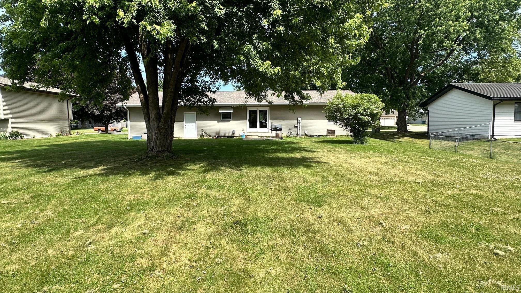 Expansive rear yard featuring a large mature tree providing shade, a stucco-clad exterior, and a double-door entry