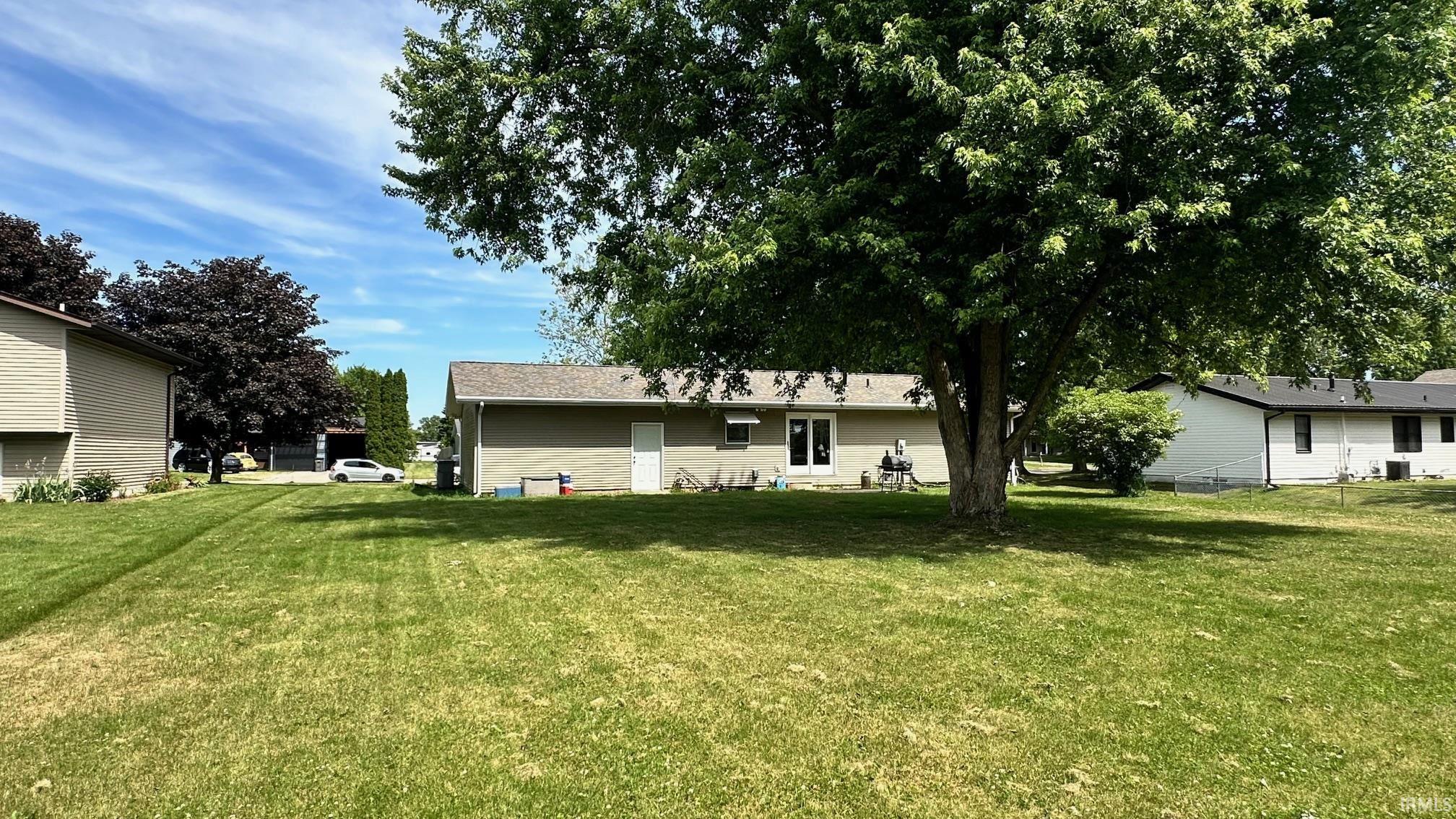 Expansive rear yard featuring a large mature tree, a single-story residence with light-colored siding, and a white rear entry door