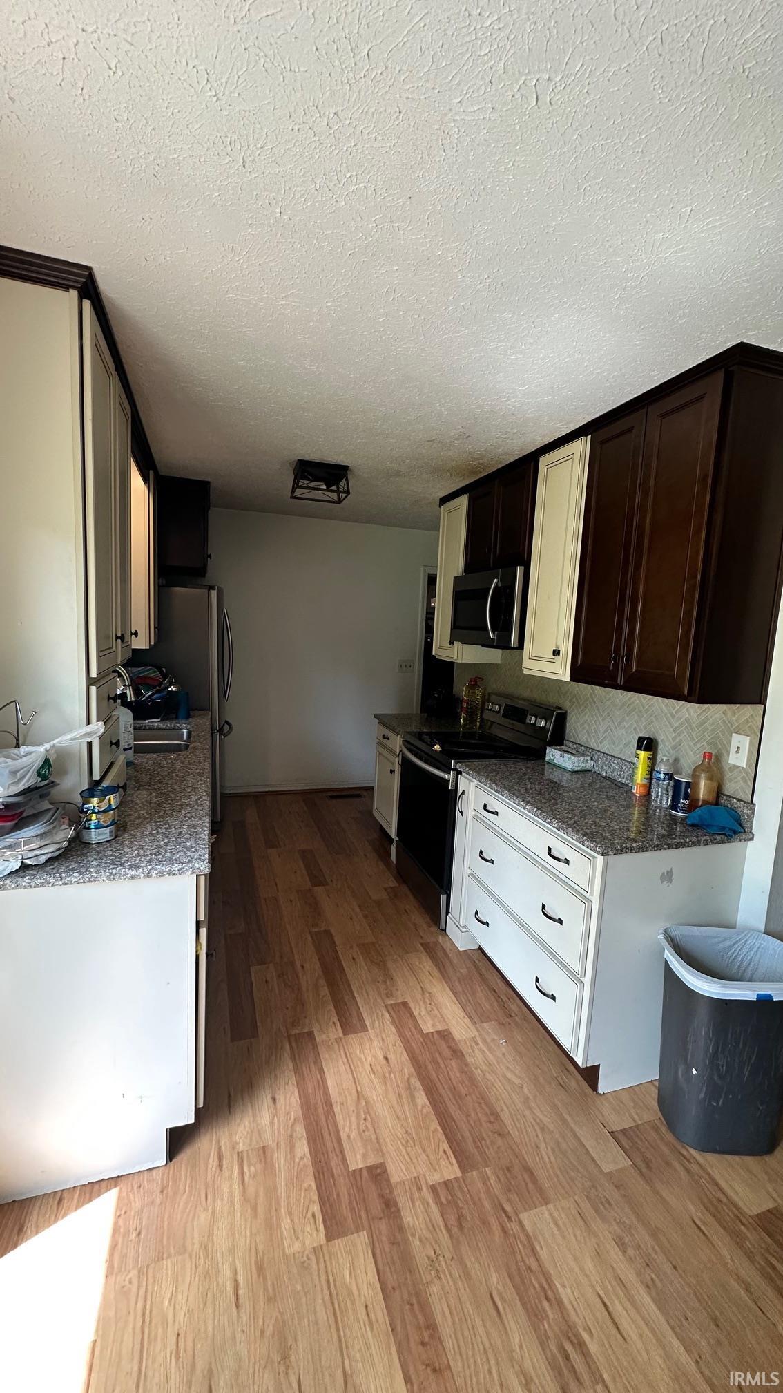 Open-concept kitchen featuring wood-finish flooring, light granite-style countertops, white lower cabinetry, and two-tone upper cabinetry with dark and light panels