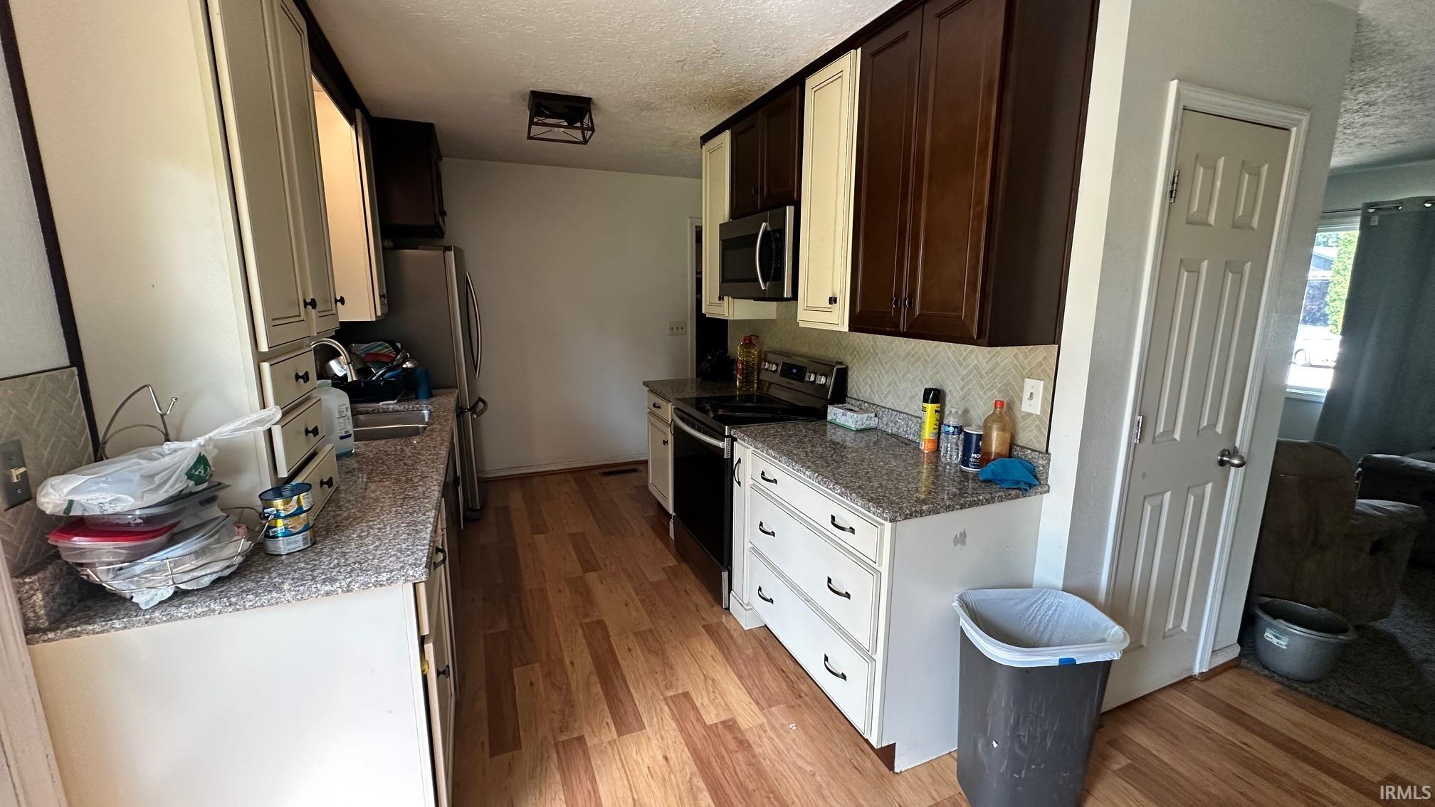 Kitchen featuring granite-style countertops, wood-finish flooring, two-tone cabinetry, stainless steel appliances, and a tiled backsplash