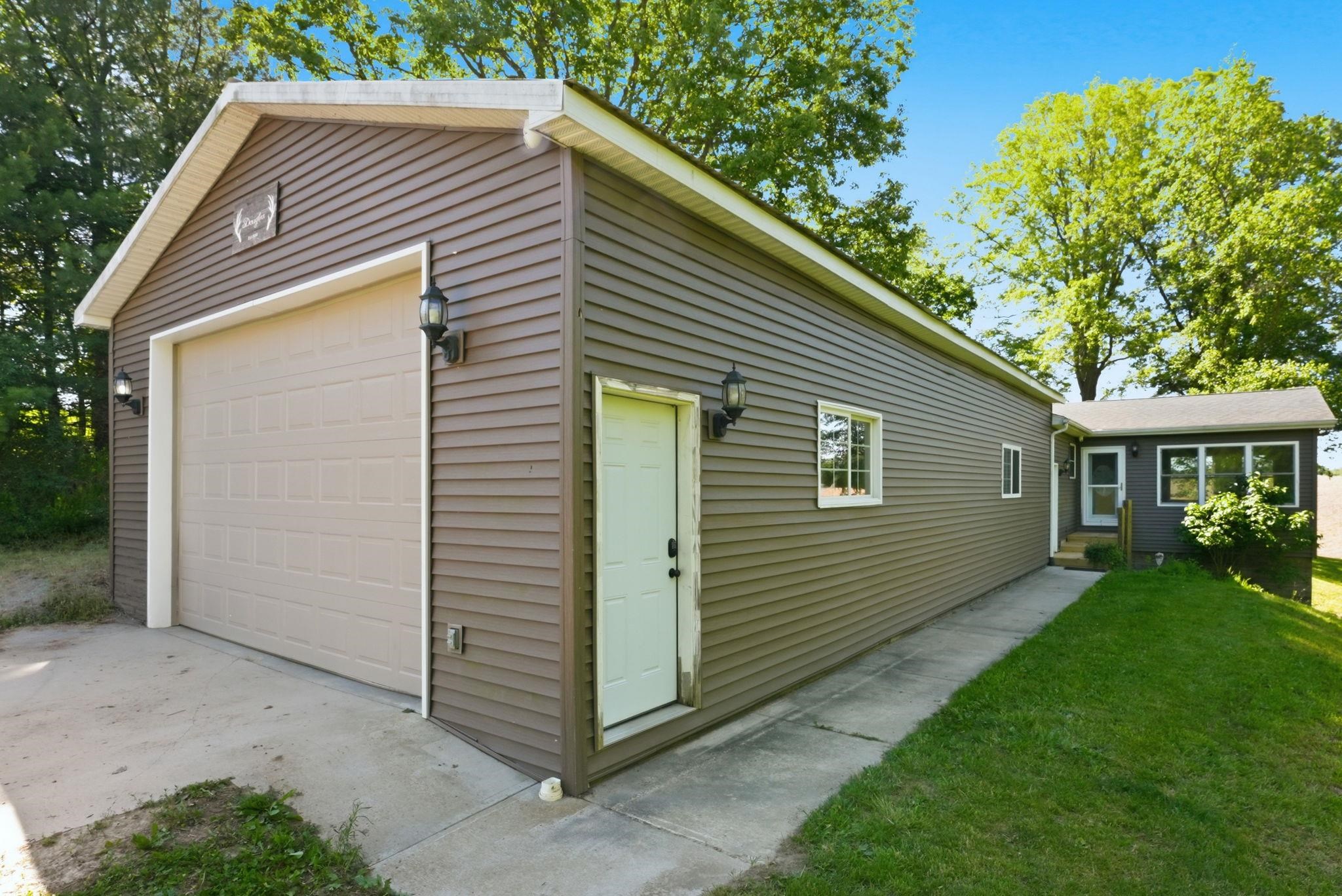 Detached garage with horizontal siding, a single beige garage door, and a separate side entry door