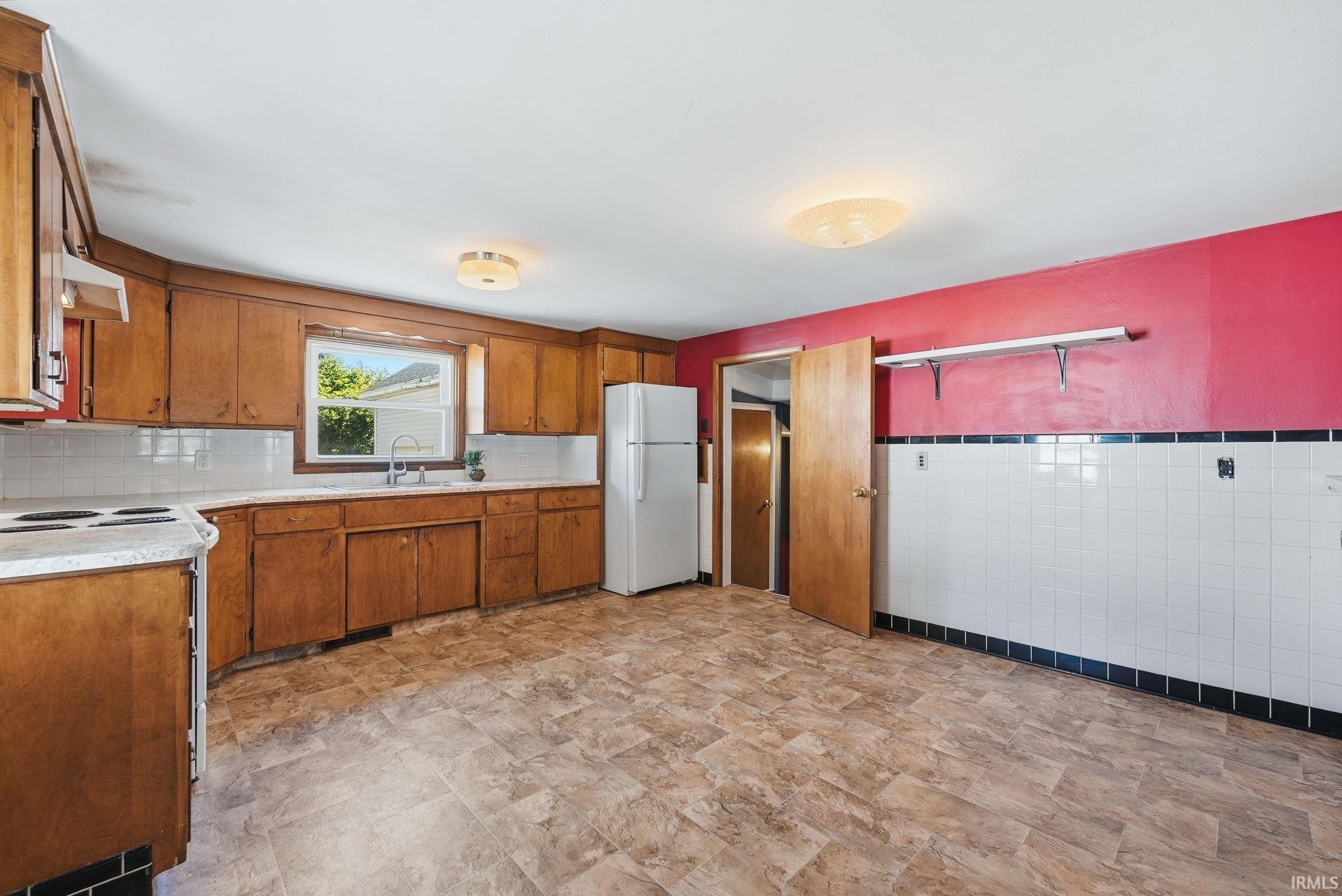 Kitchen featuring wood cabinetry, white tile backsplash, and a window above the sink