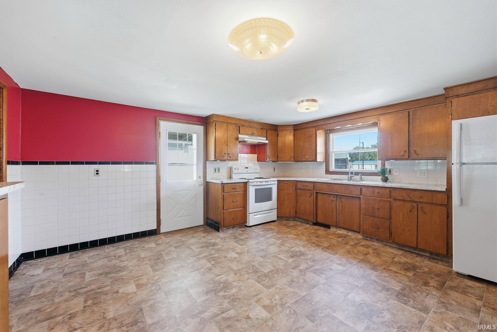 Spacious kitchen featuring extensive wood cabinetry, white appliances, and a double-basin sink