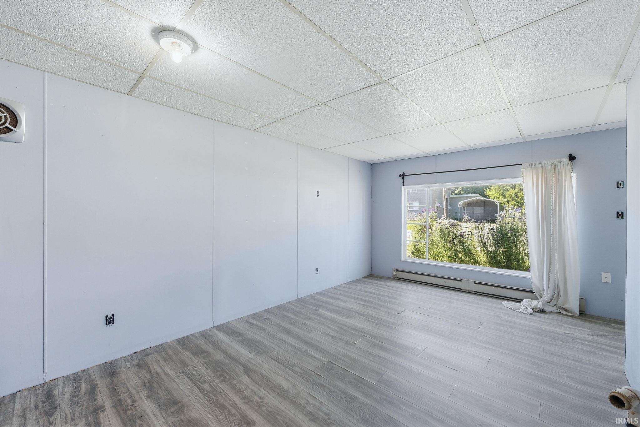 Spacious room featuring wood-finish flooring, light blue paneling, a large window, and ceiling-mounted lighting