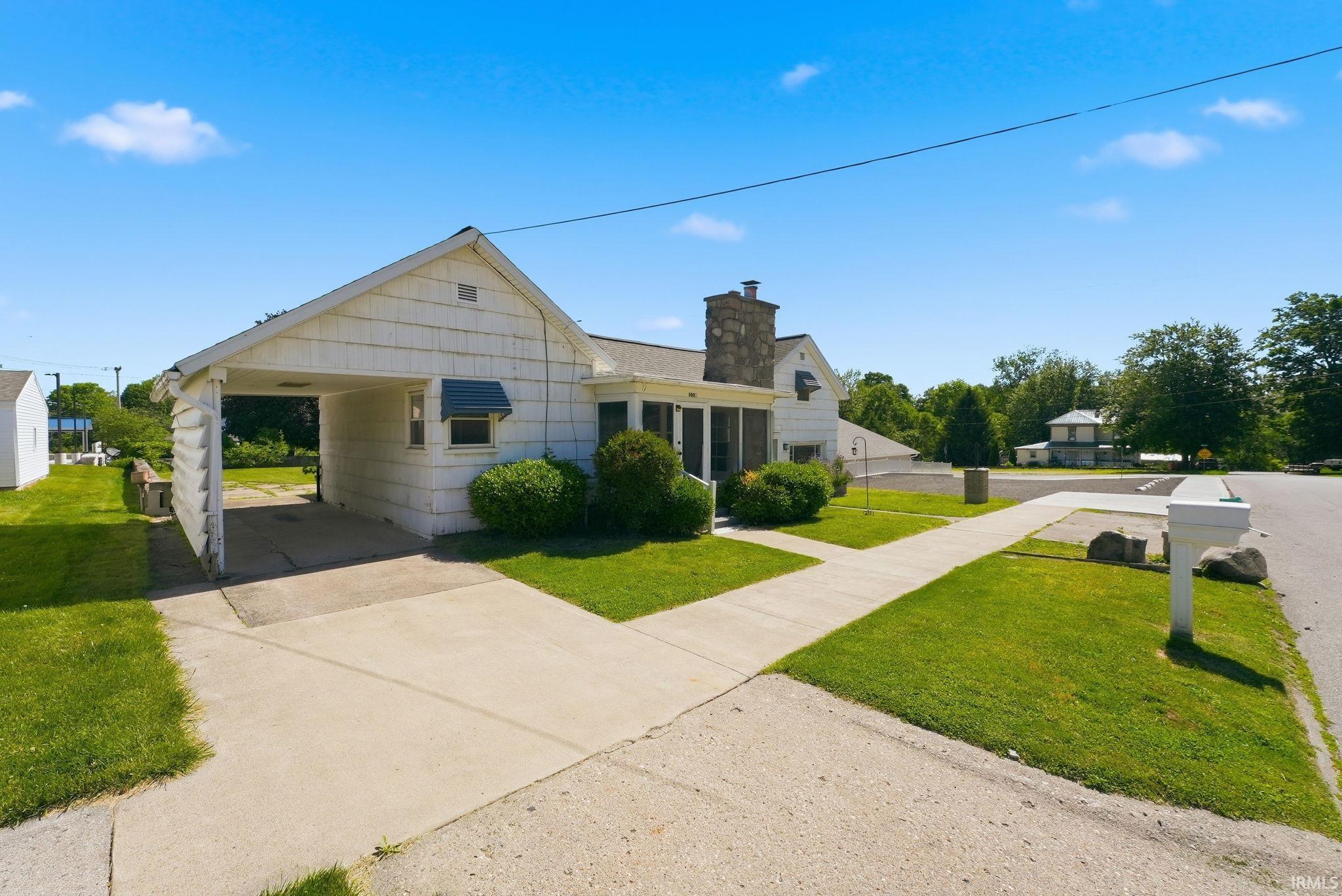 White siding residence with a covered carport, stone chimney, and a screened-in porch