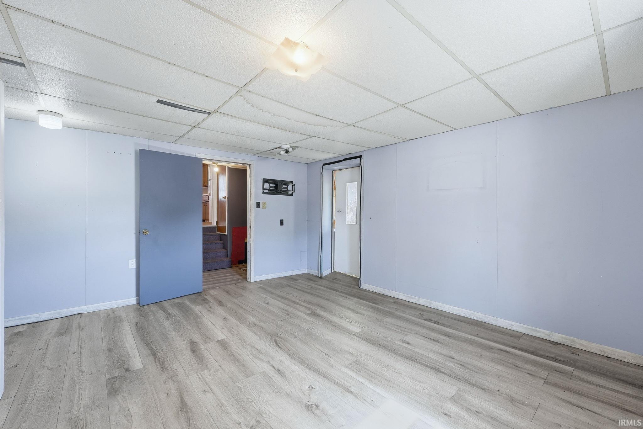 Spacious room featuring wood-finish flooring, light blue panel walls, and a white drop ceiling with recessed lighting