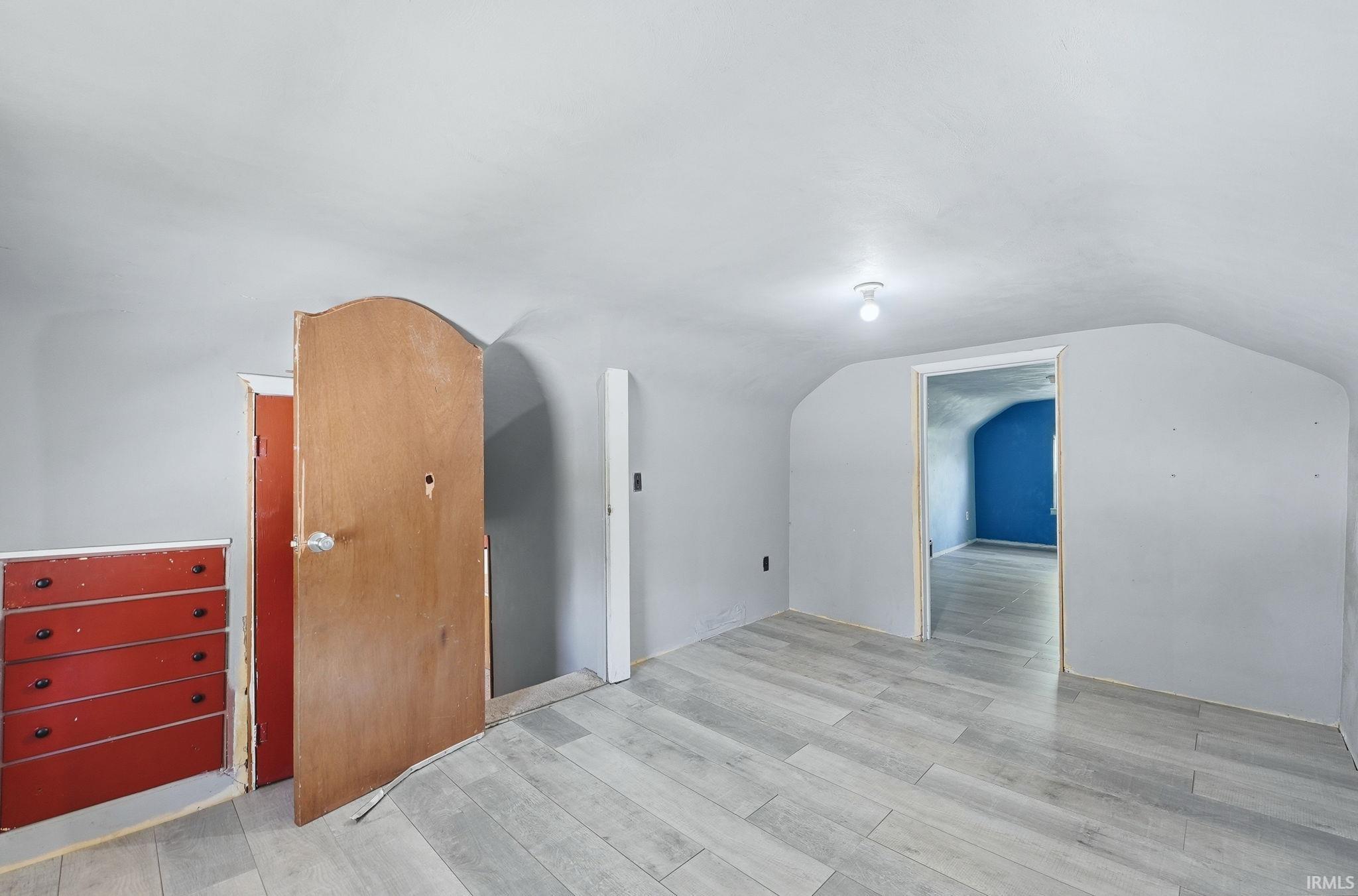 Room featuring wood-finish flooring, gently sloped ceilings, and neutral-toned walls