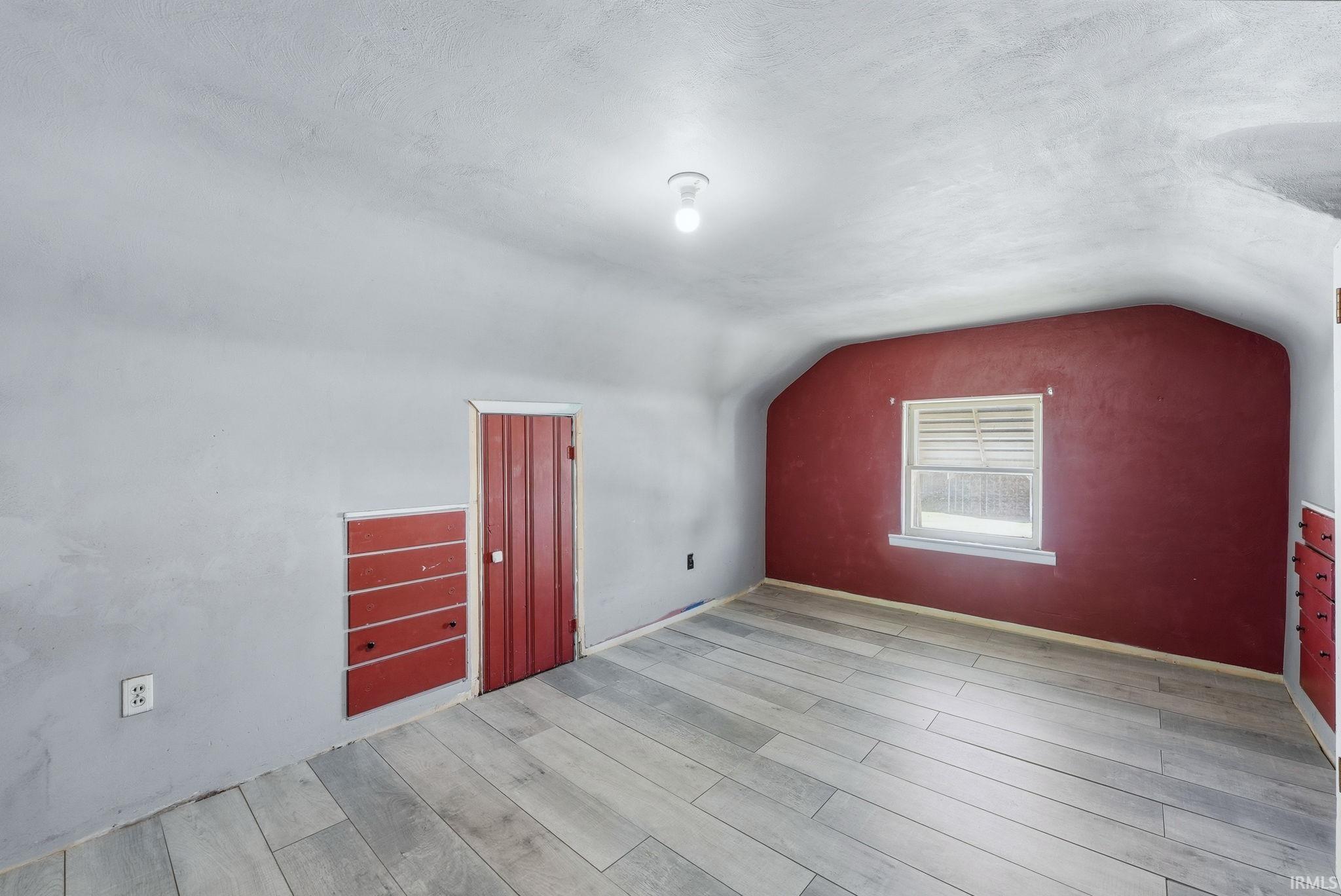 Room featuring wood-finish flooring, a window with horizontal blinds, and a built-in red door