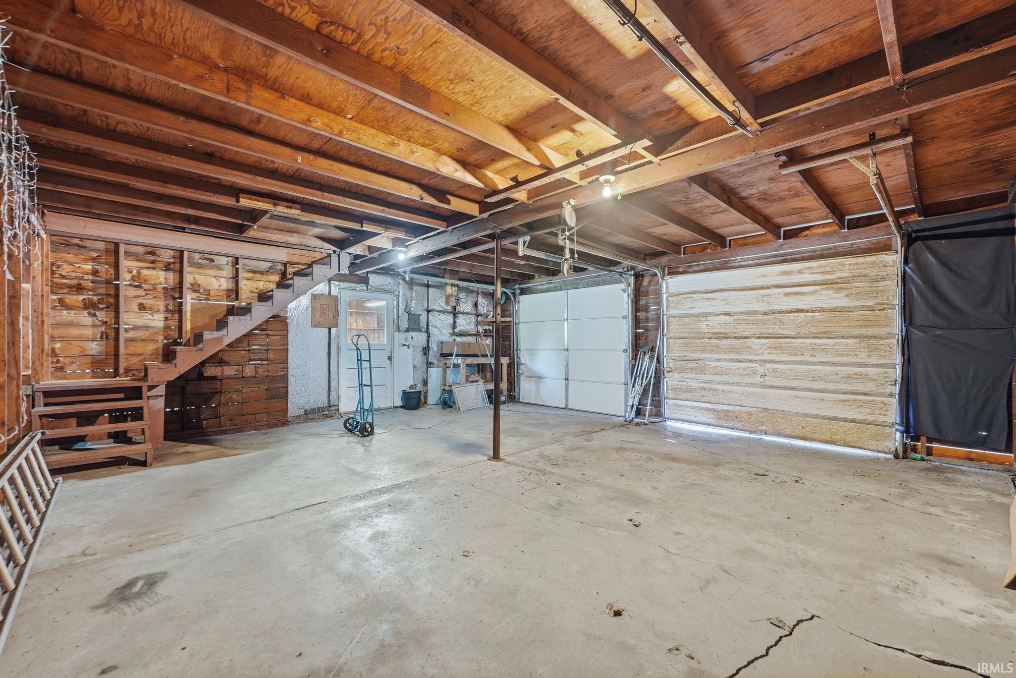 Multi-bay garage featuring concrete flooring, exposed wood beam ceiling, and a visible staircase