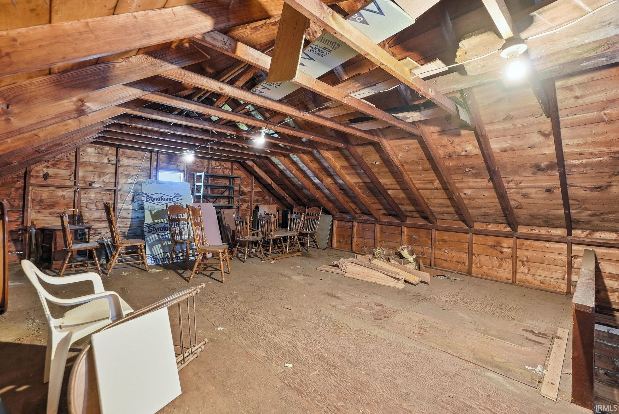 Spacious attic featuring exposed wood beams and wood plank walls