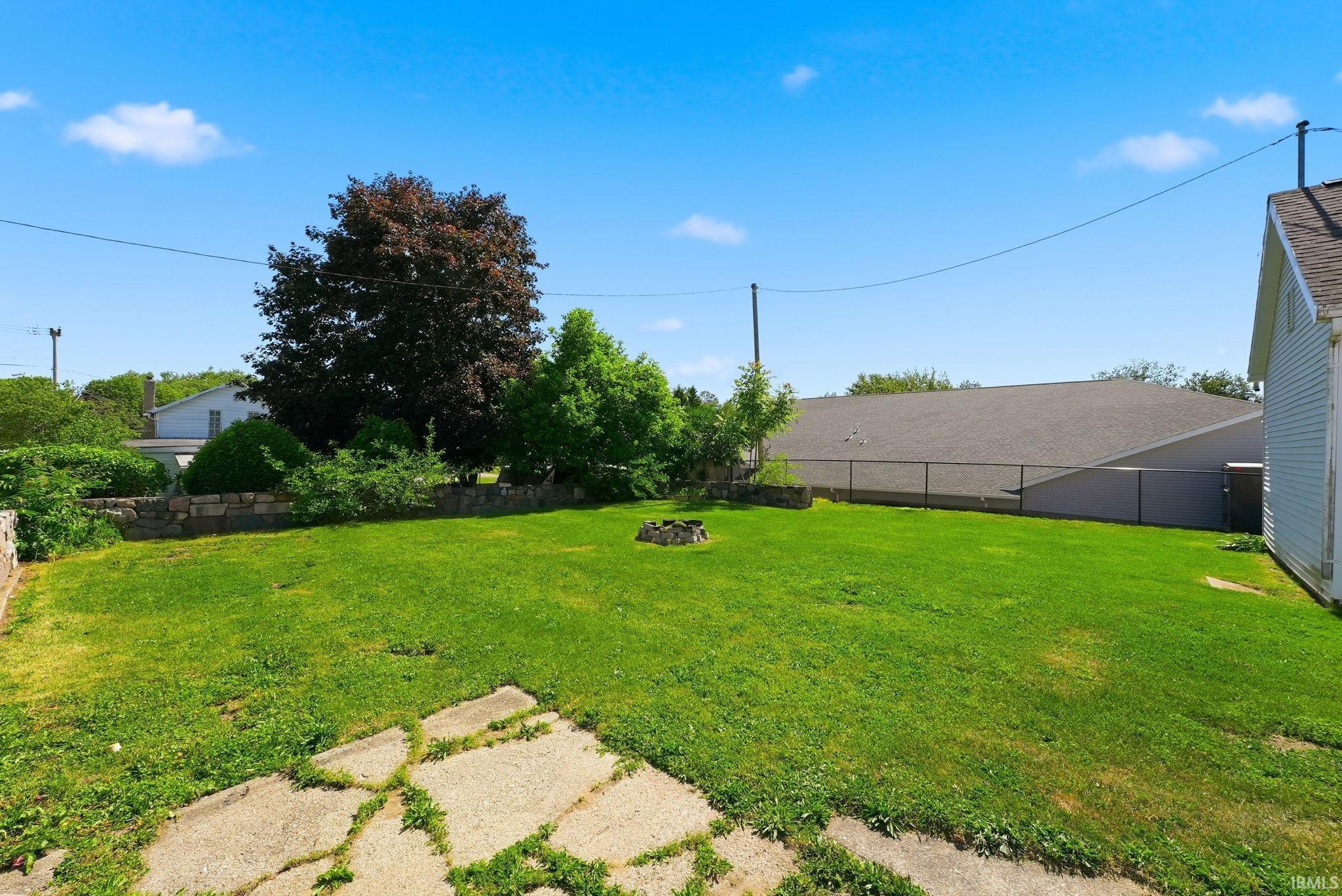 Spacious backyard featuring a large grass lawn, mature trees, and a stone retaining wall