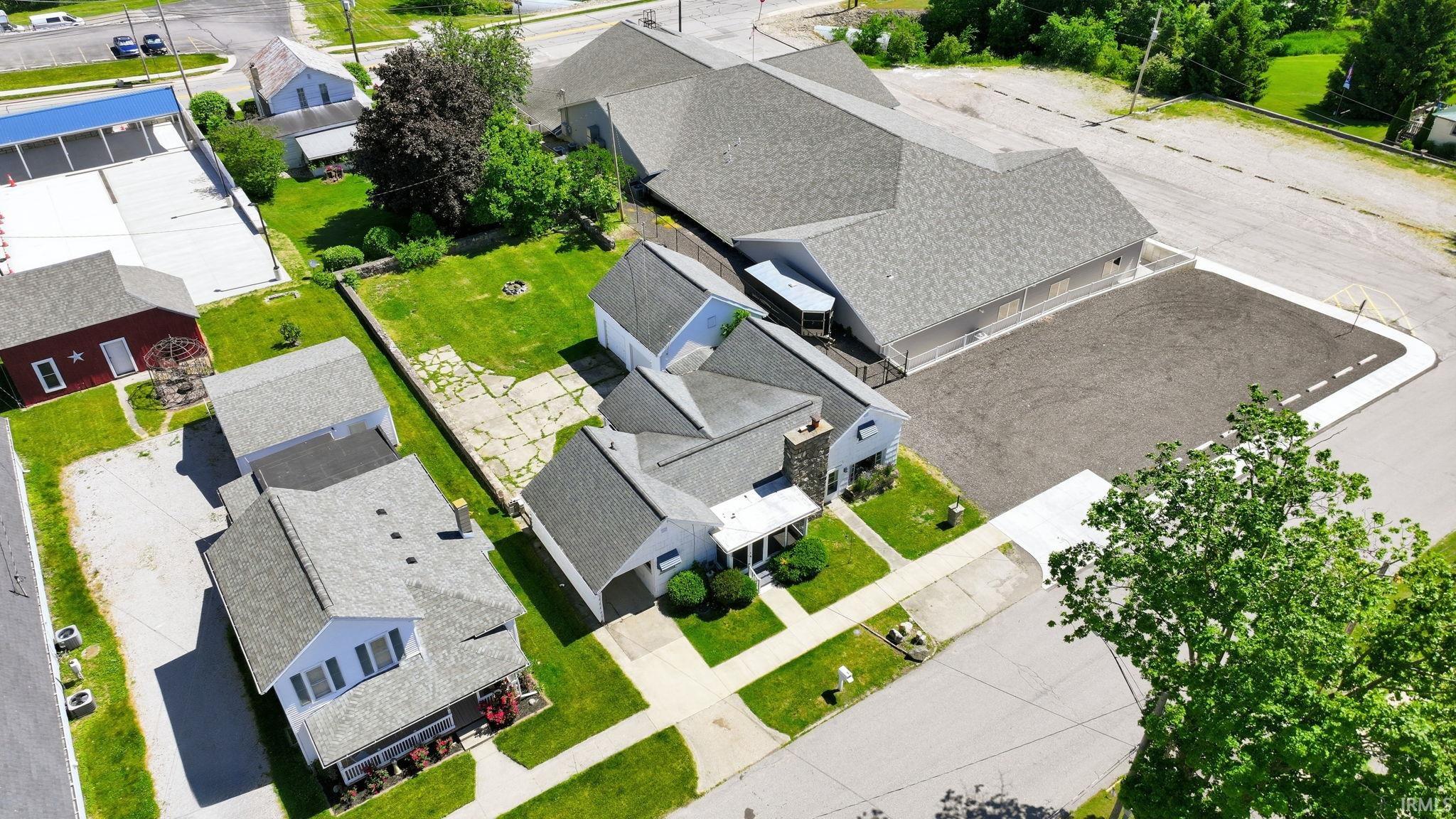 Property featuring a spacious commercial building with a gray shingle roof and a large, paved parking area