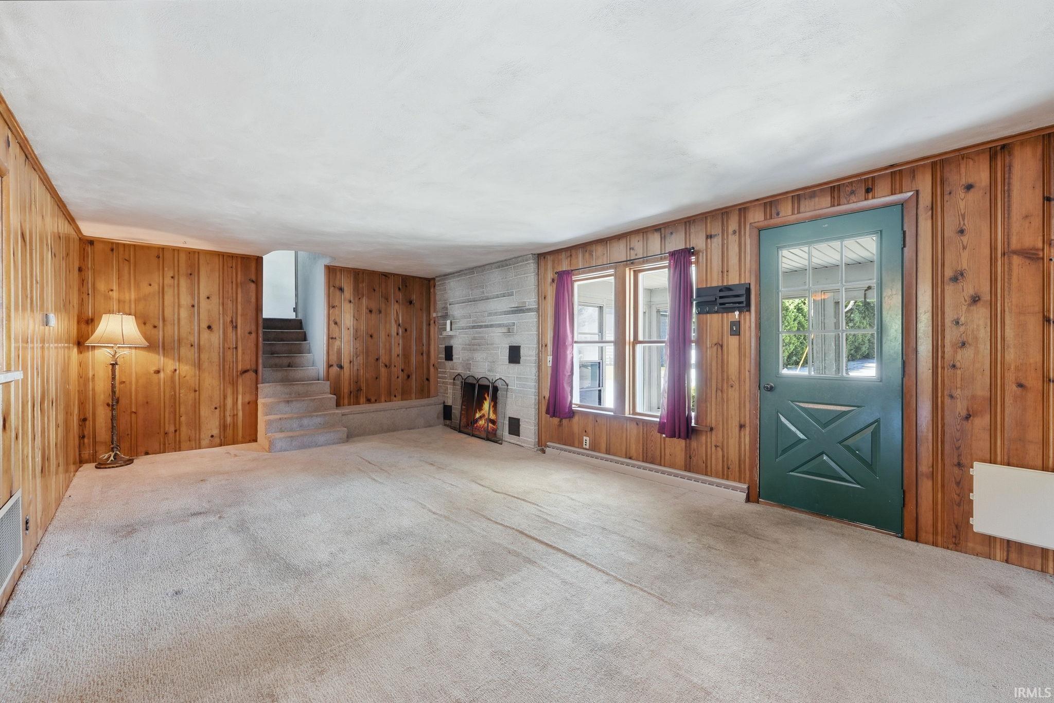 Carpeted interior space featuring wood paneling, a stone fireplace, and a partial staircase