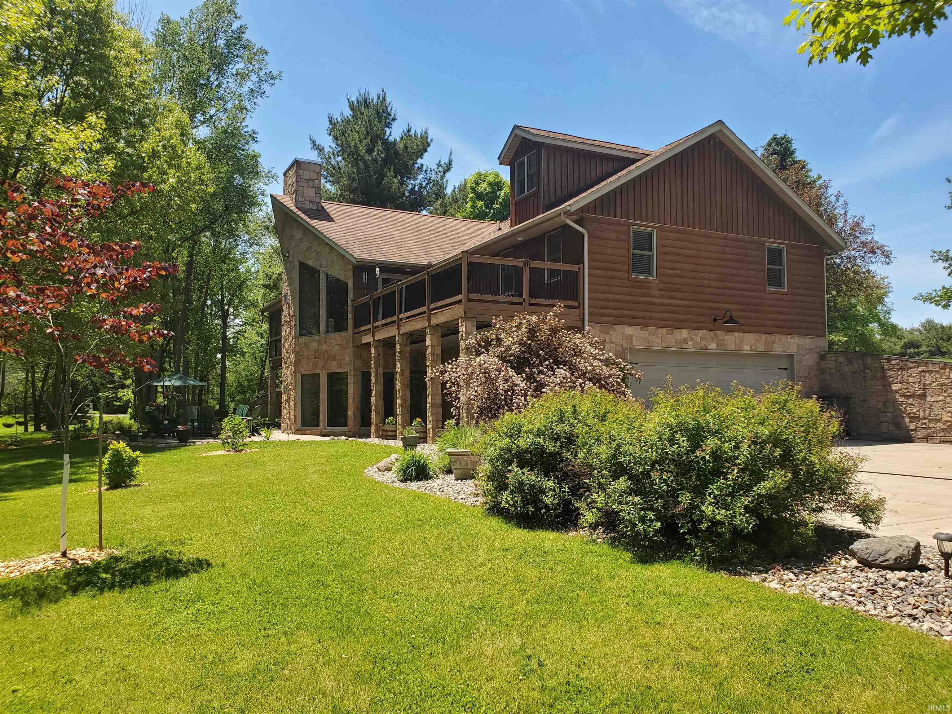 Rustic-style residence featuring a stone and wood-finish facade, an integrated garage, a screened-in upper deck, and a stone chimney
