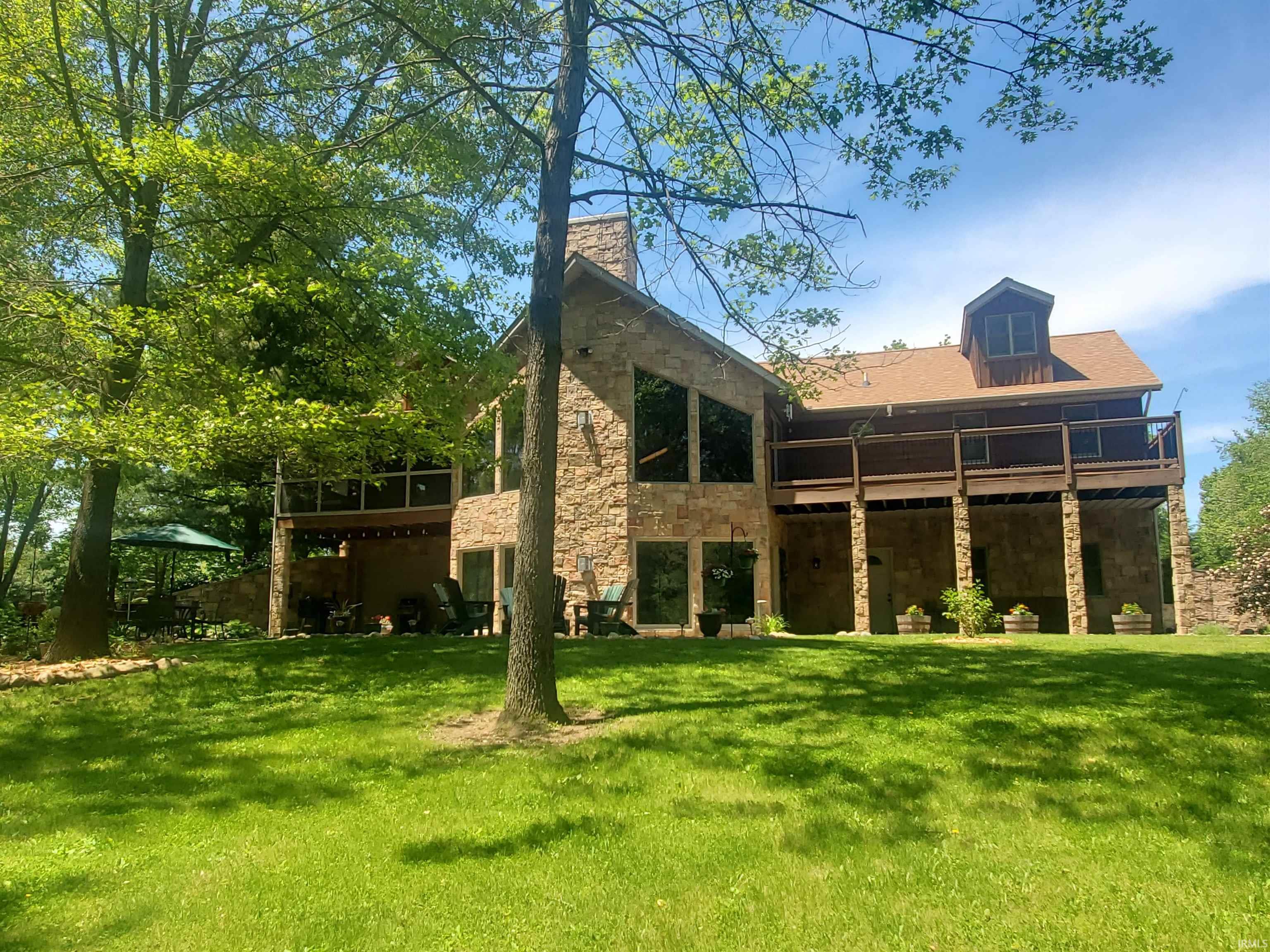 Stone-clad exterior featuring multiple levels, a dormer window, and an expansive upper-level deck with a wood railing