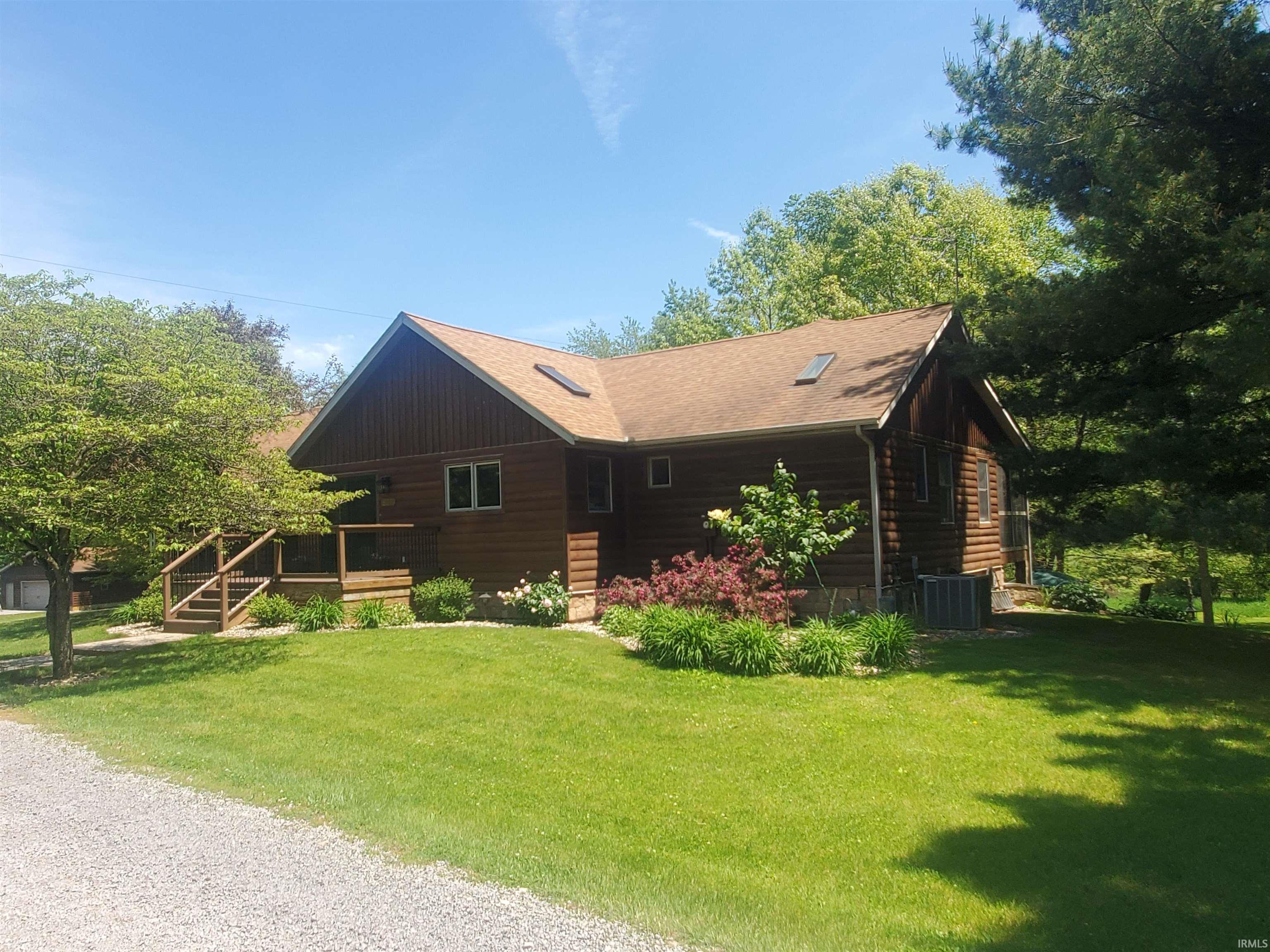 Wood-sided exterior featuring an inviting deck with railings, a prominent gable roofline, and a gravel driveway