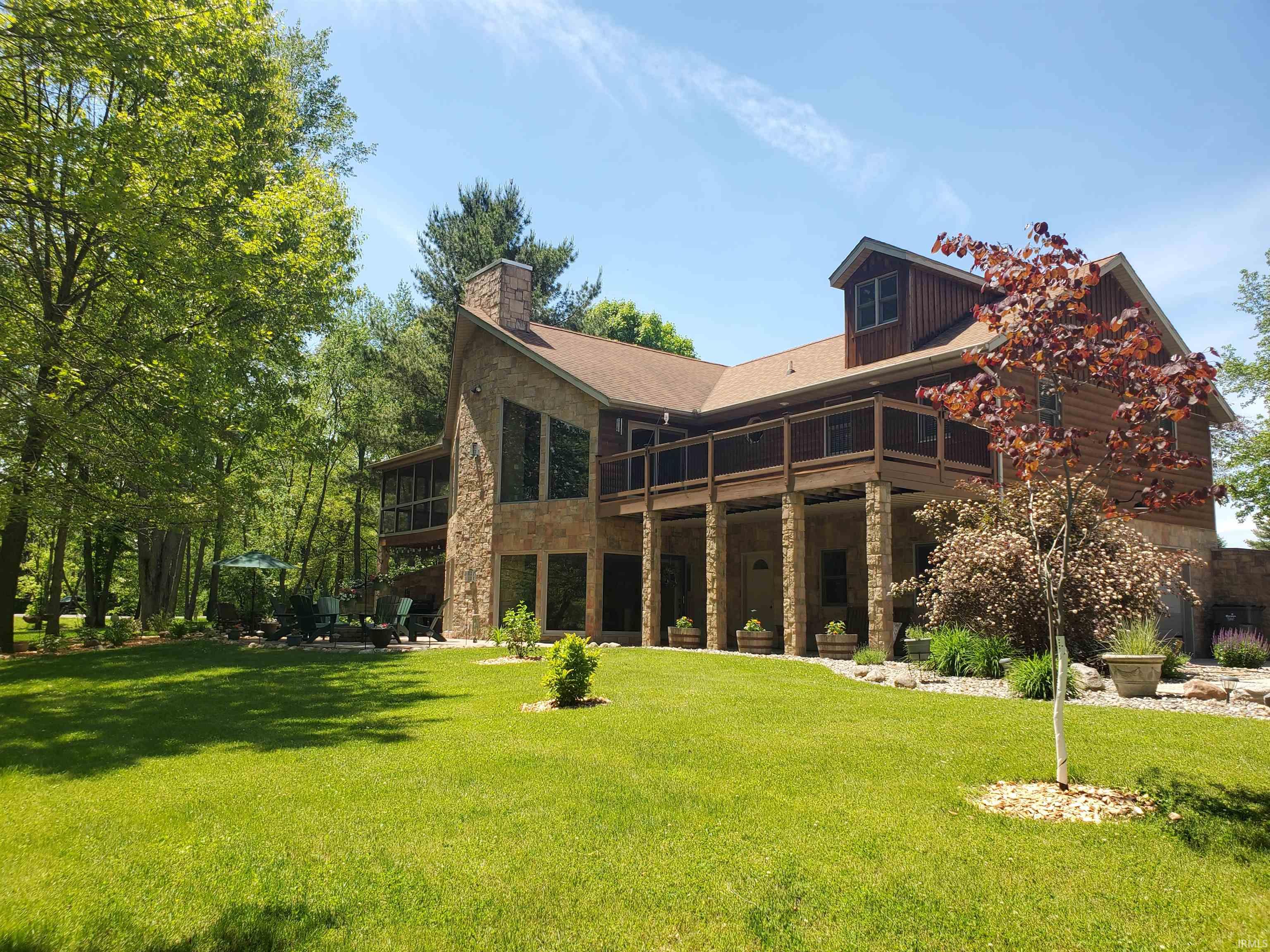 Multi-level residence featuring stone and wood siding, a screened porch, and an expansive lawn