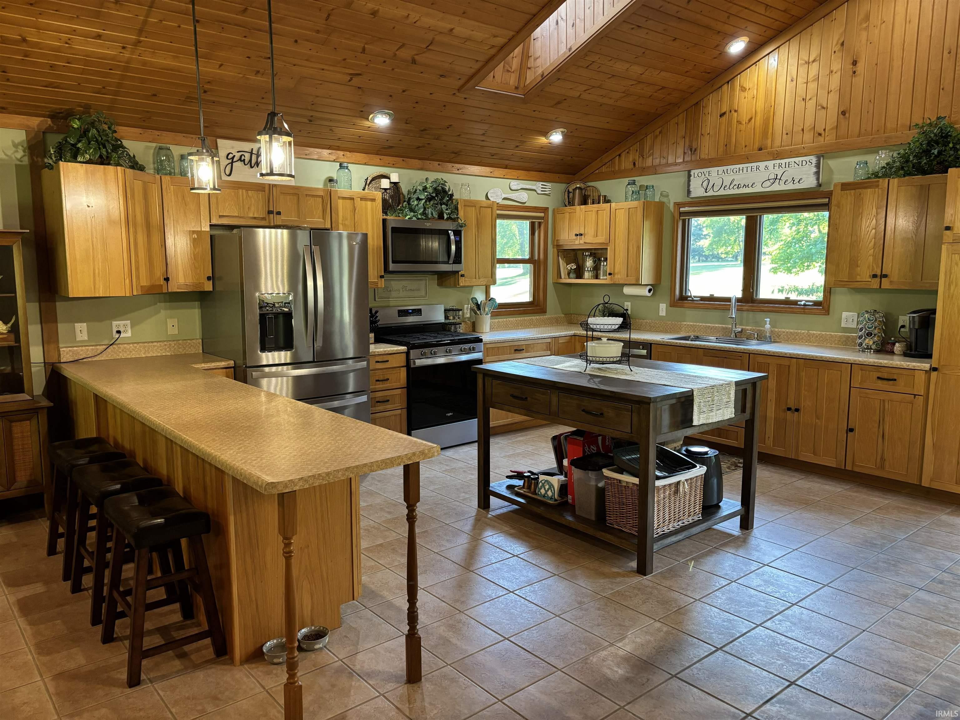 Kitchen featuring wood plank vaulted ceilings with skylight, oak cabinetry, stainless steel appliances, a breakfast bar, and a central island