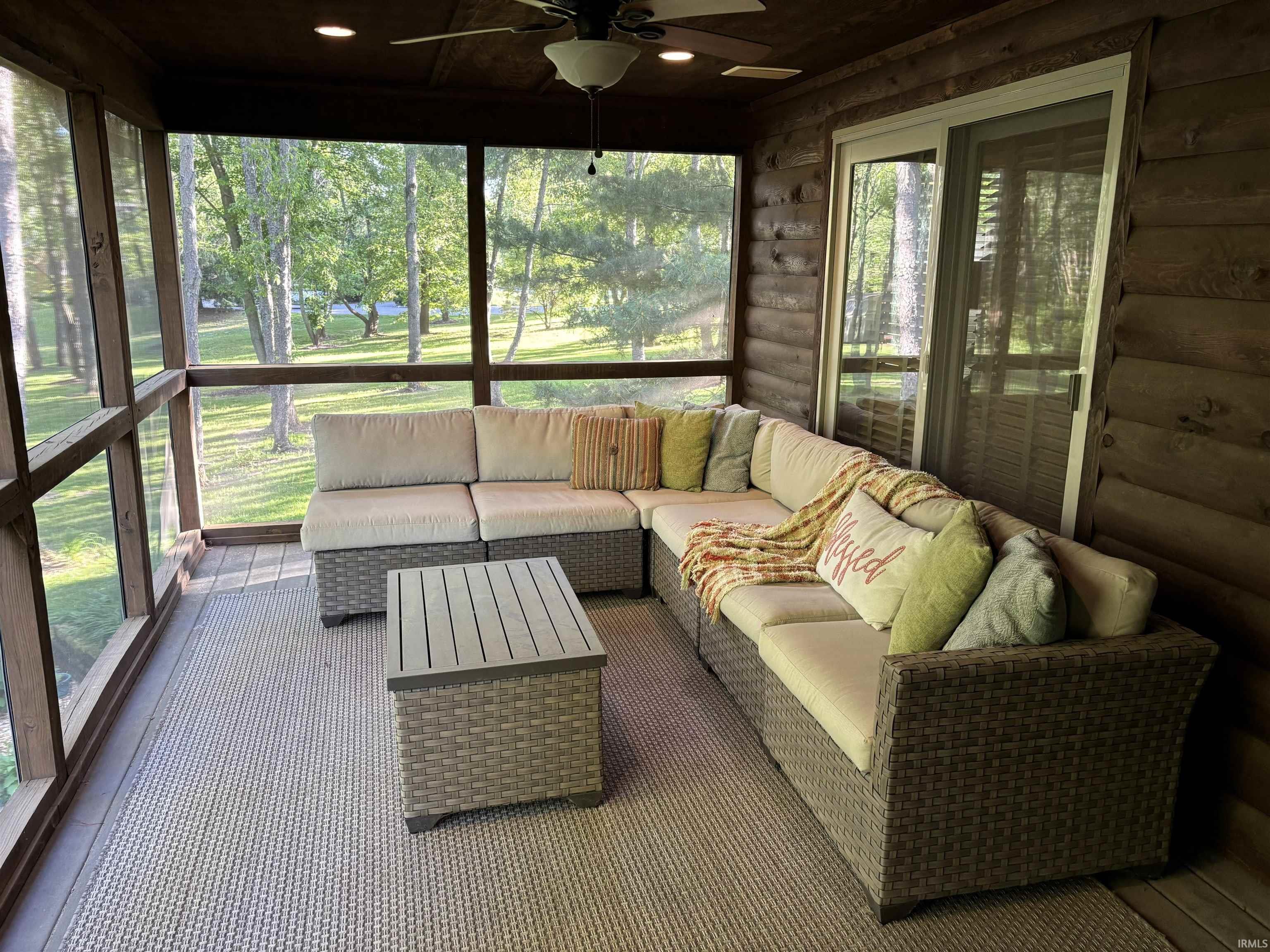 Spacious screened porch featuring log cabin-style walls, wood-finish flooring, and a ceiling fan with integrated lighting