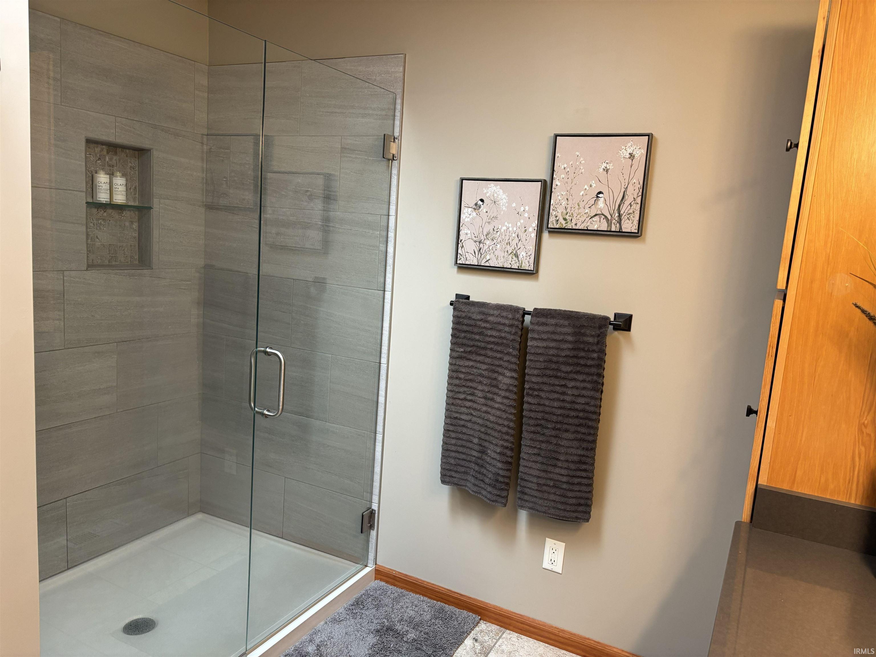 Glass-enclosed shower featuring large format grey tile, a built-in shower niche with a glass shelf, and a white shower pan