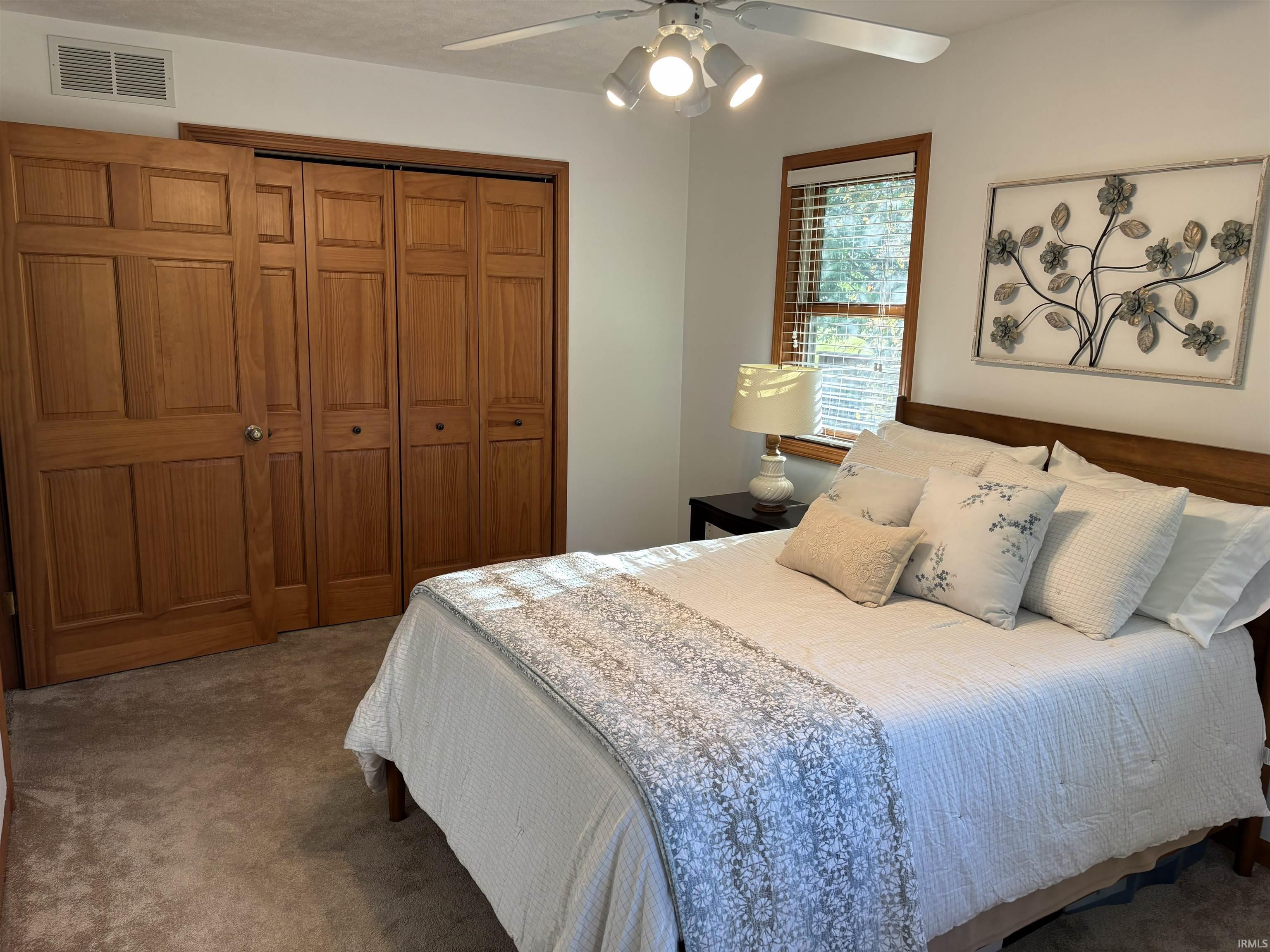 Room featuring wood-finish bi-fold and sliding closet doors, carpeted flooring, a window with horizontal blinds, and a ceiling fan with integrated lighting