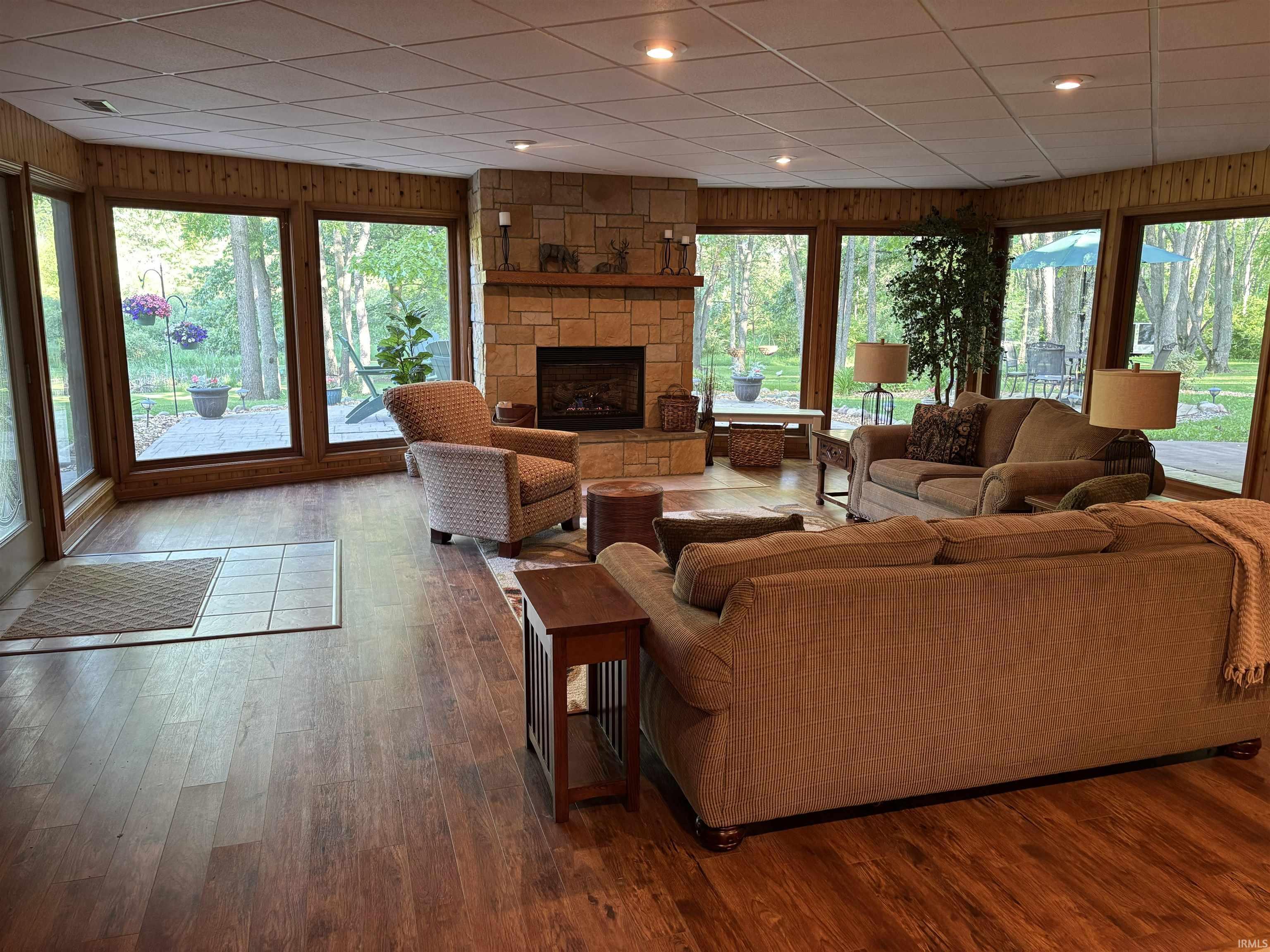 Living area featuring a stone fireplace with a wood mantel, wood-finish flooring, and extensive window views