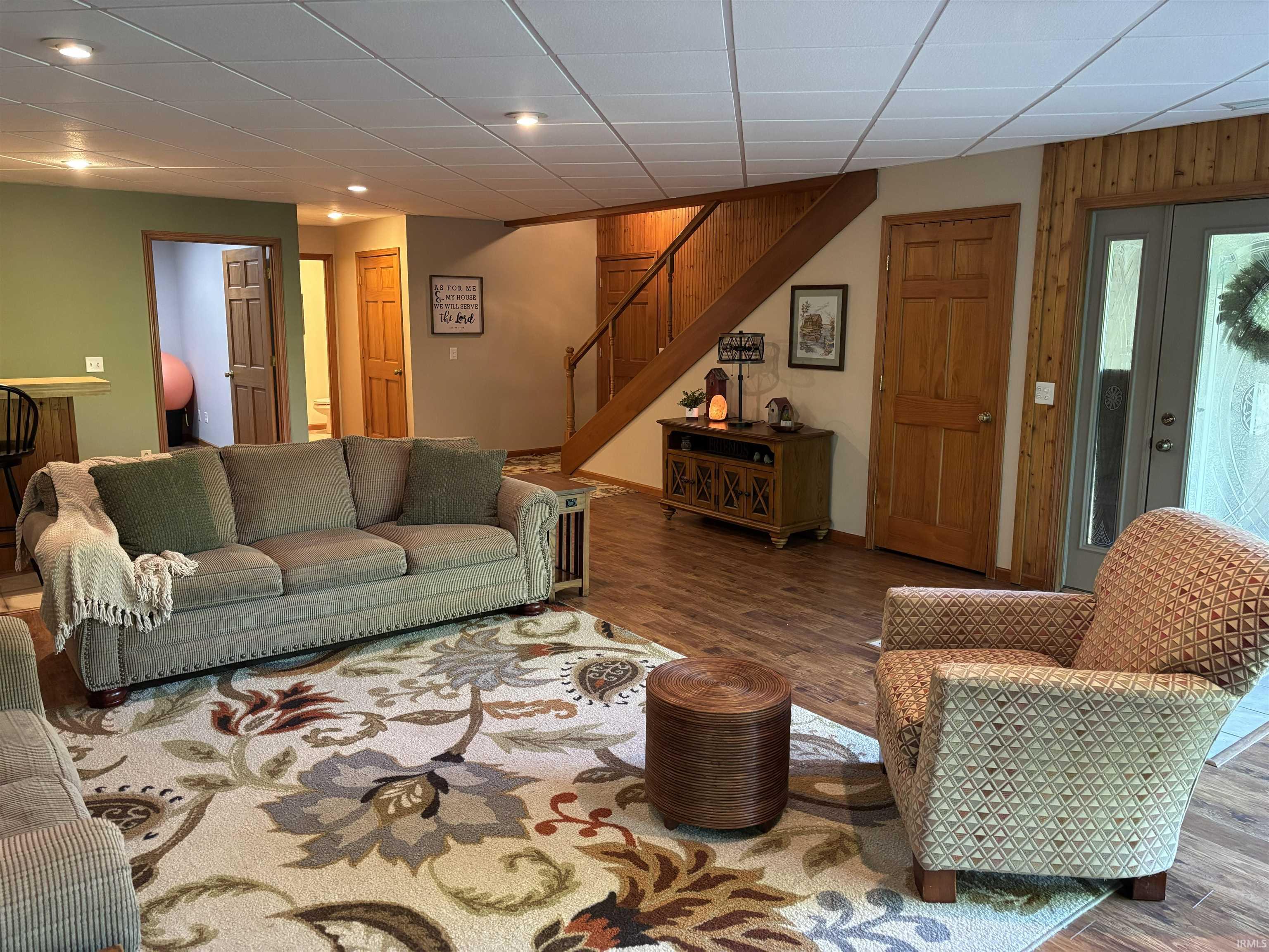 Spacious room featuring wood-finish flooring, a wood staircase with railing, recessed lighting, and a drop ceiling