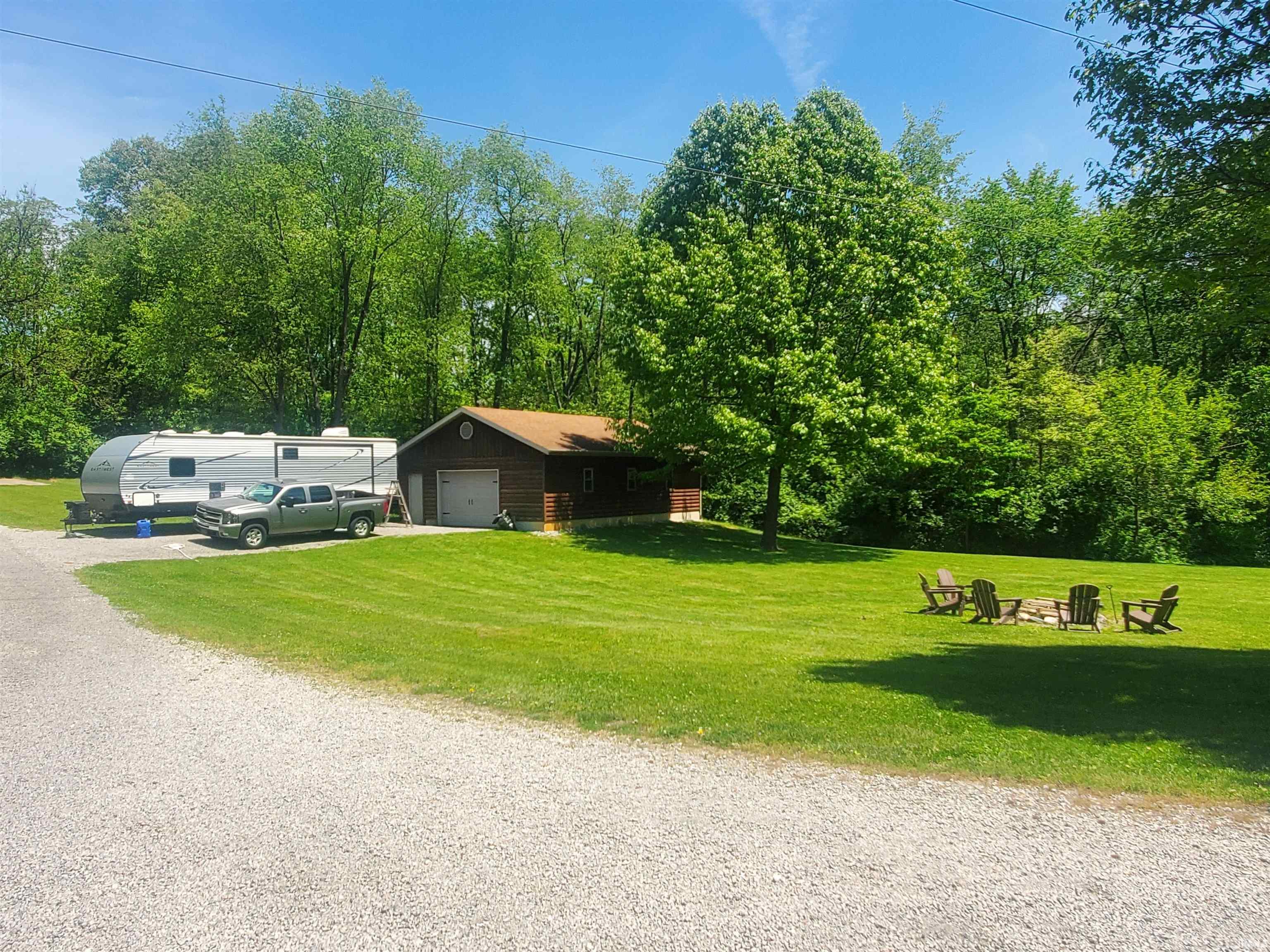 Expansive green lawn with a gravel driveway and surrounding mature trees
