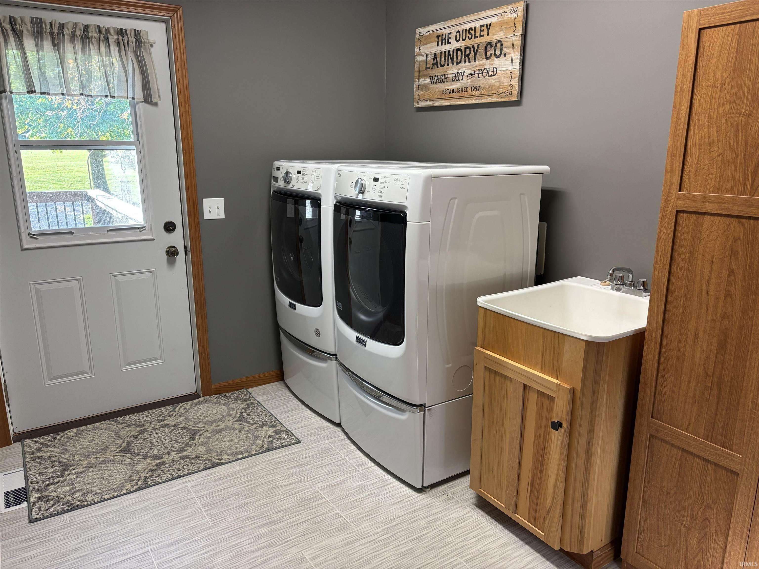 Utility room featuring light-toned plank-style flooring, a built-in utility sink with wood-finish cabinetry, and a white exterior door with an upper window