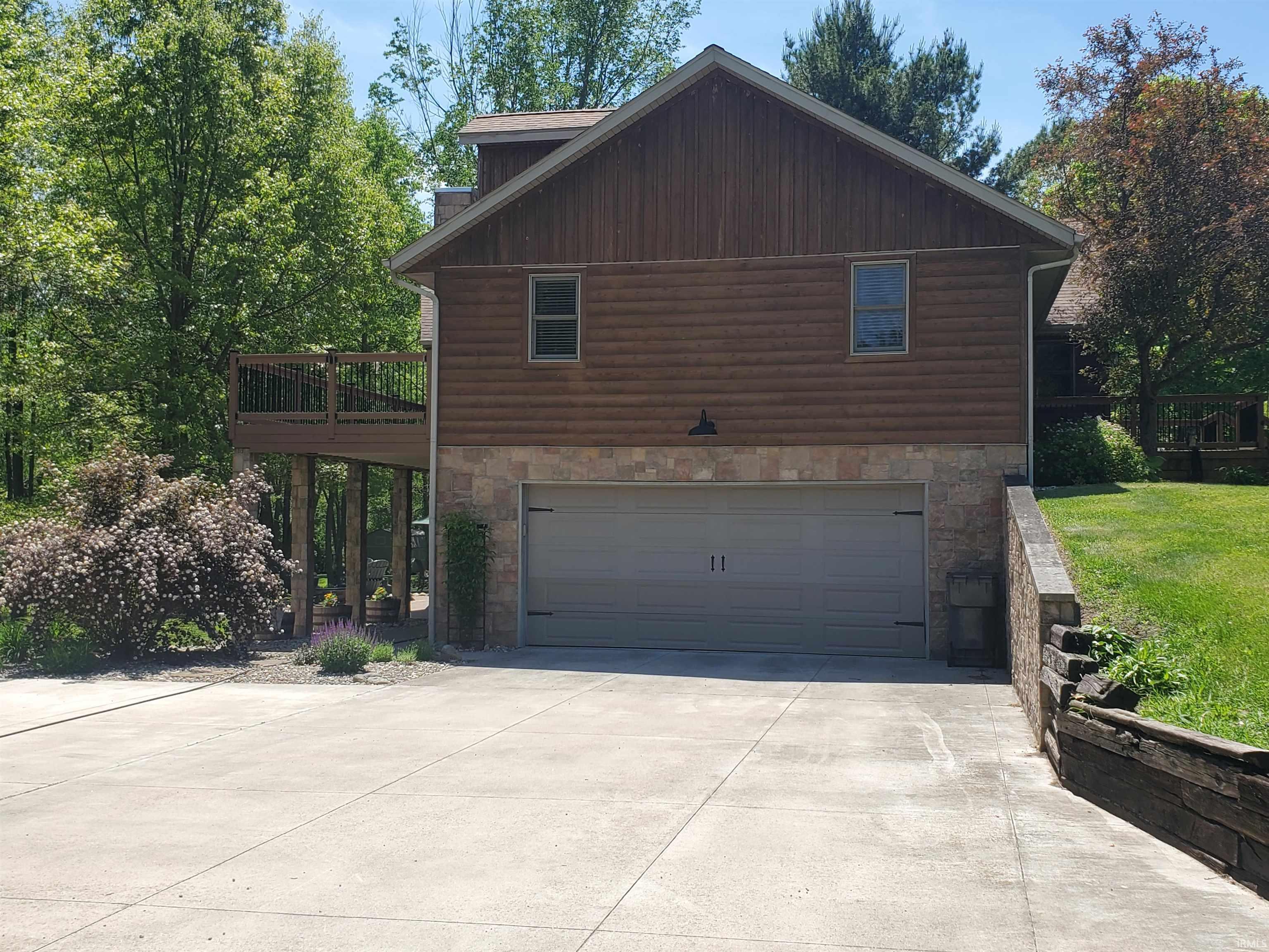 Exterior featuring a two-car garage, stone veneer, wood siding, and an upper-level deck with dark railings