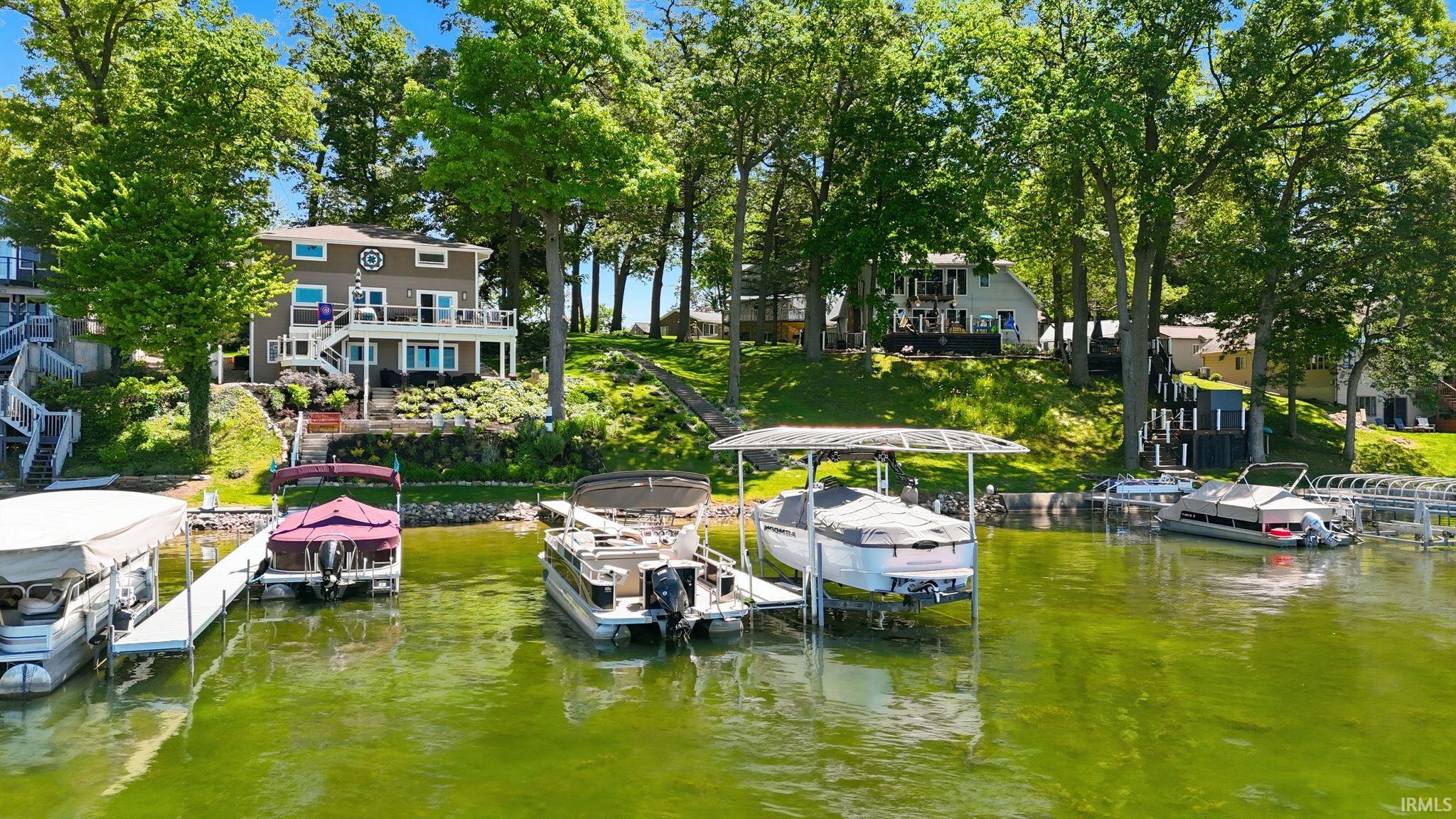 Waterfront property featuring a two-story residence with multiple balconies, mature trees, a tiered landscape, and direct water access with multiple docks