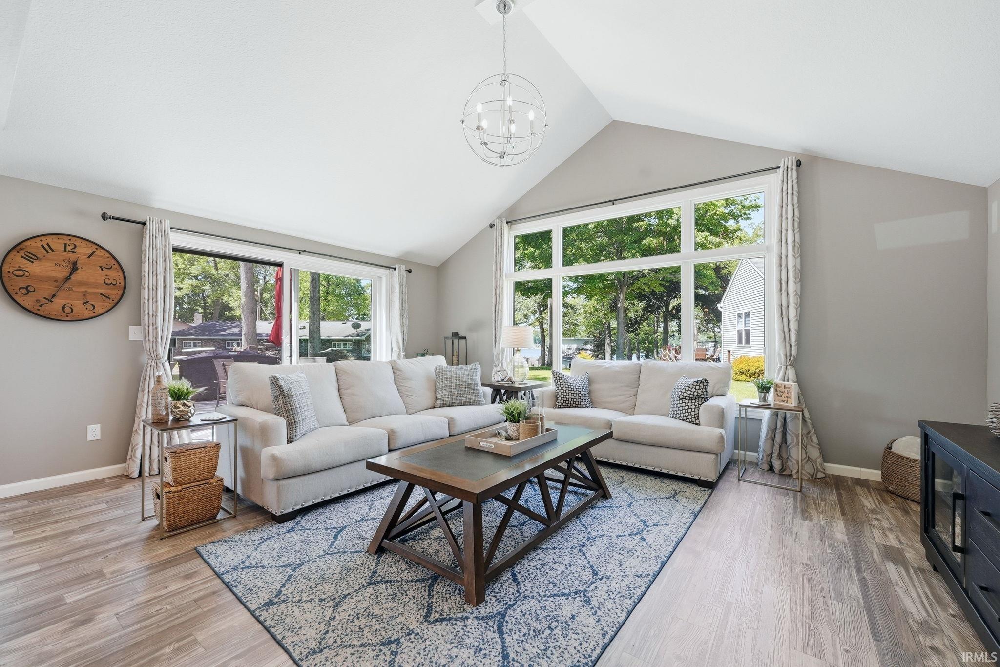 Living area with vaulted ceilings, wood-finish flooring, a contemporary chandelier, and large windows offering exterior views