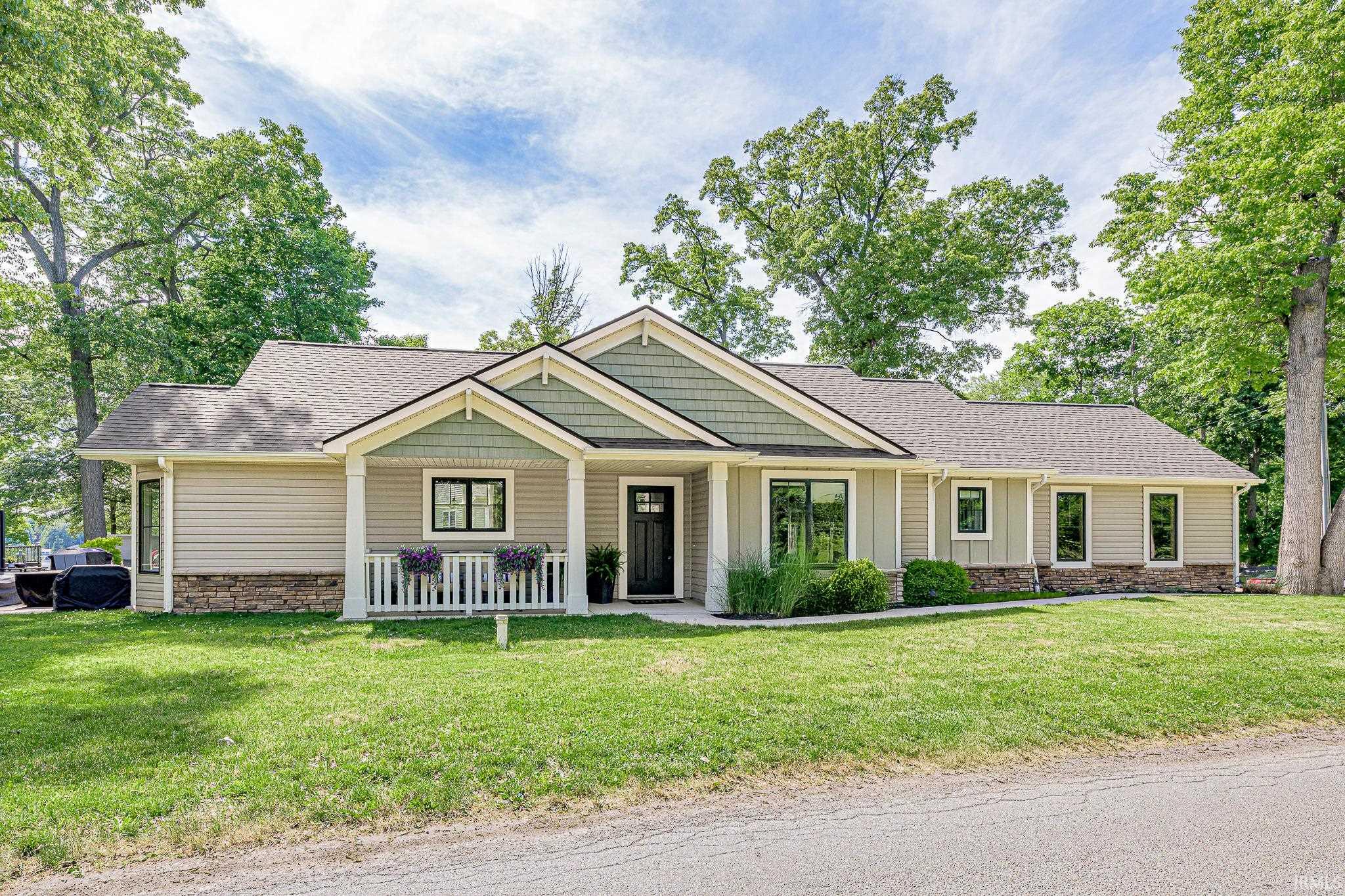 Ranch-style residence featuring light-colored siding, a dark asphalt shingle roof, and a stone veneer foundation
