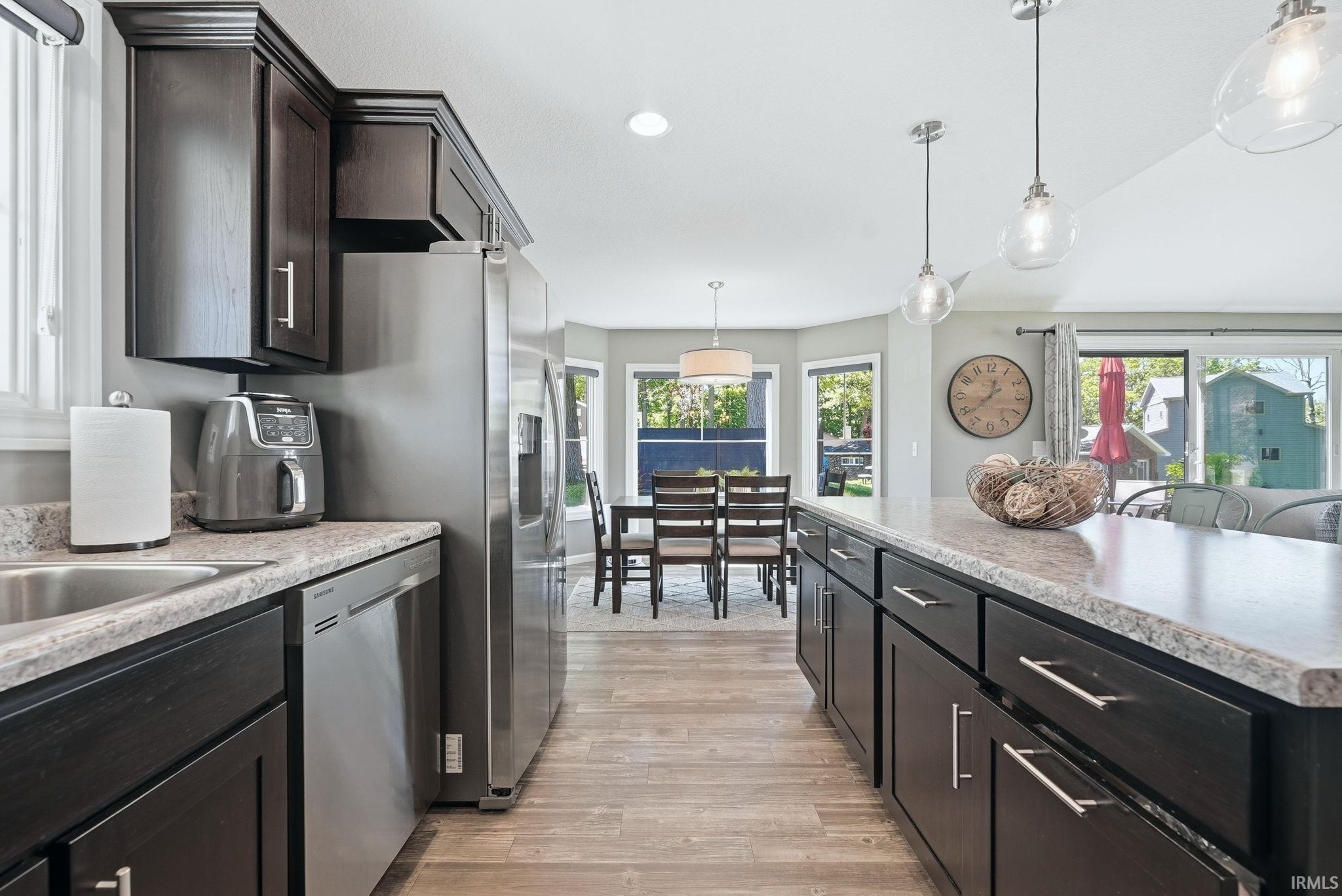 Kitchen featuring dark wood cabinetry, stainless steel appliances, light speckled countertops, and wood-finish flooring