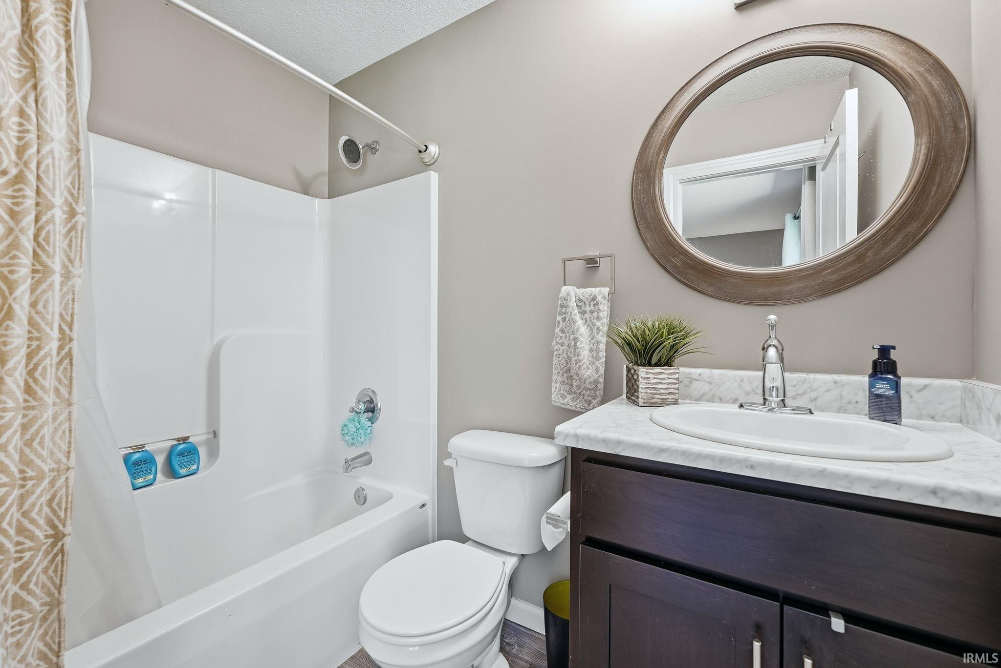 Full bathroom featuring a white tub and shower combination with chrome fixtures, a white toilet, and a vanity with a white countertop and dark wood-finish cabinetry