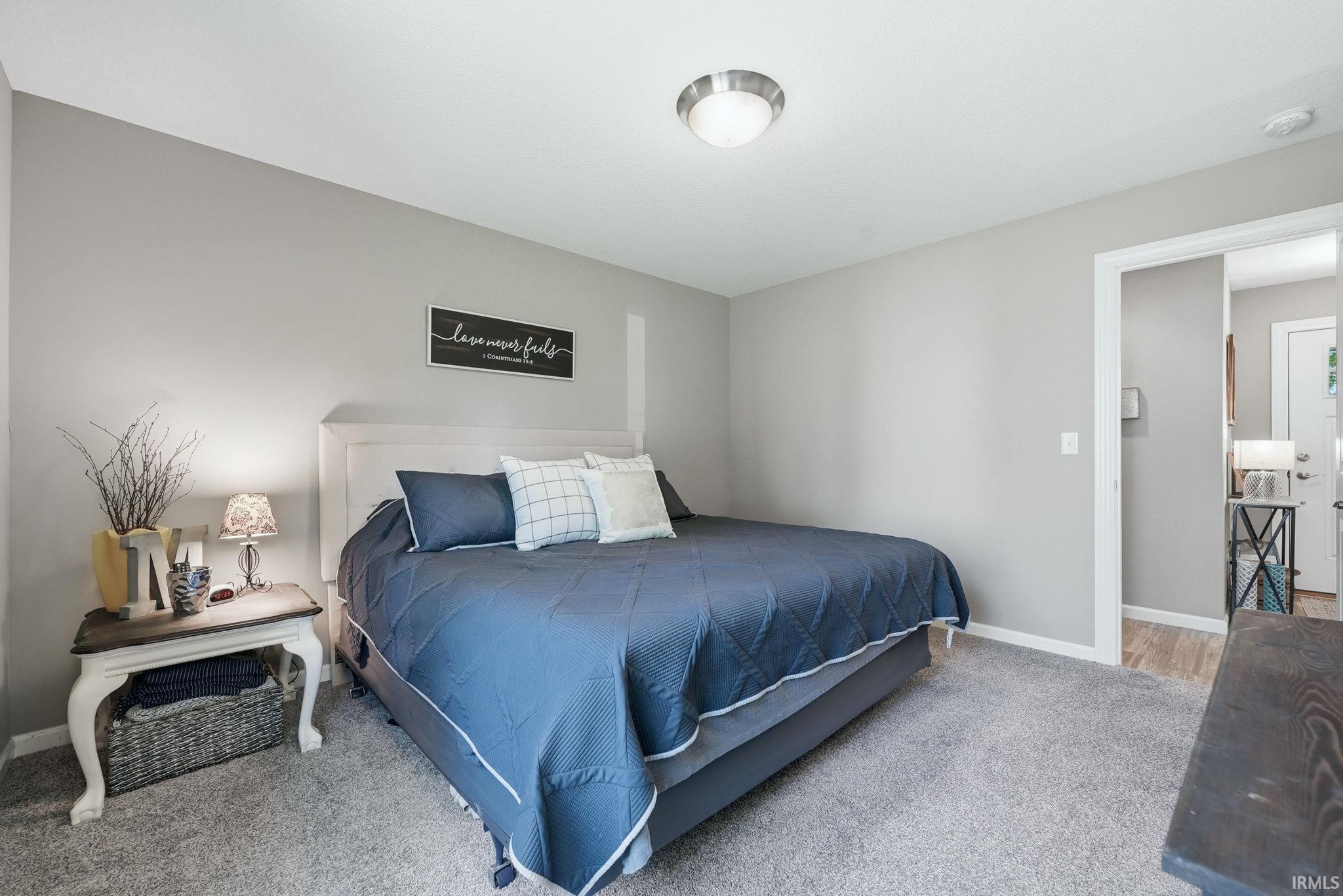 Carpeted bedroom featuring neutral-toned walls, a white headboard, and a flush mount ceiling light