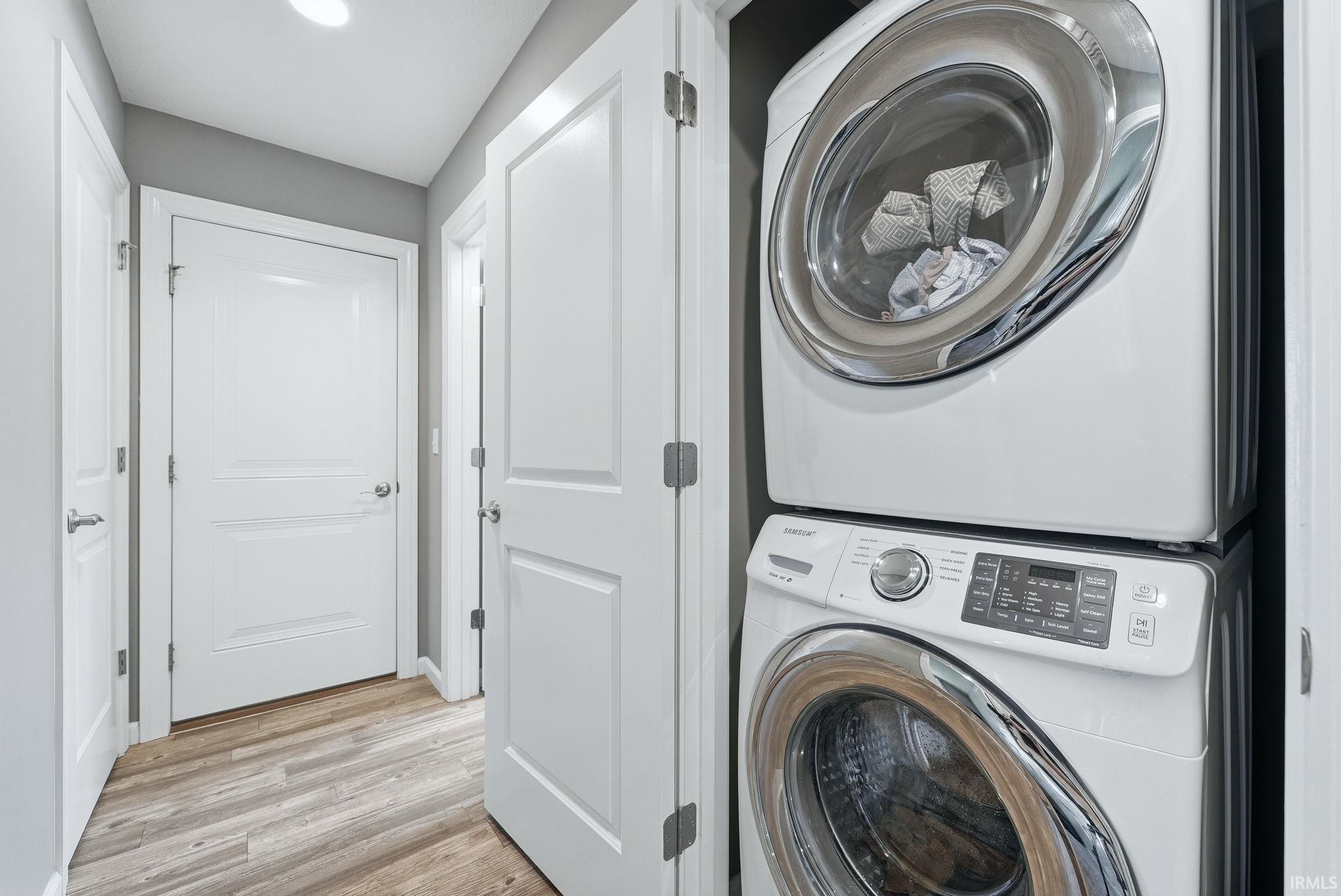 Dedicated laundry closet featuring a stacked white washer and dryer unit, complemented by light wood-finish flooring and white paneled doors