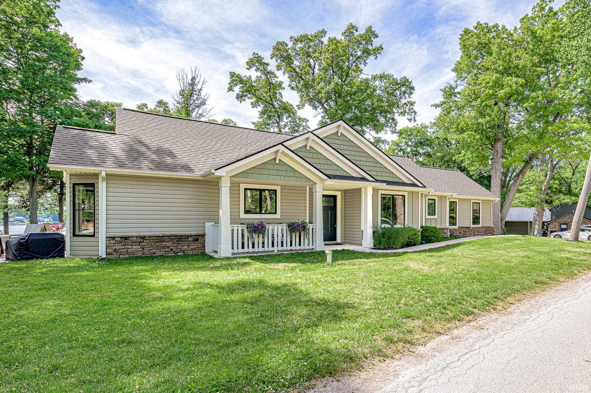 Contemporary residence featuring a covered front porch with white railing, a dark entry door, light siding with stone accents, a multi-pitched roofline, and established landscaping