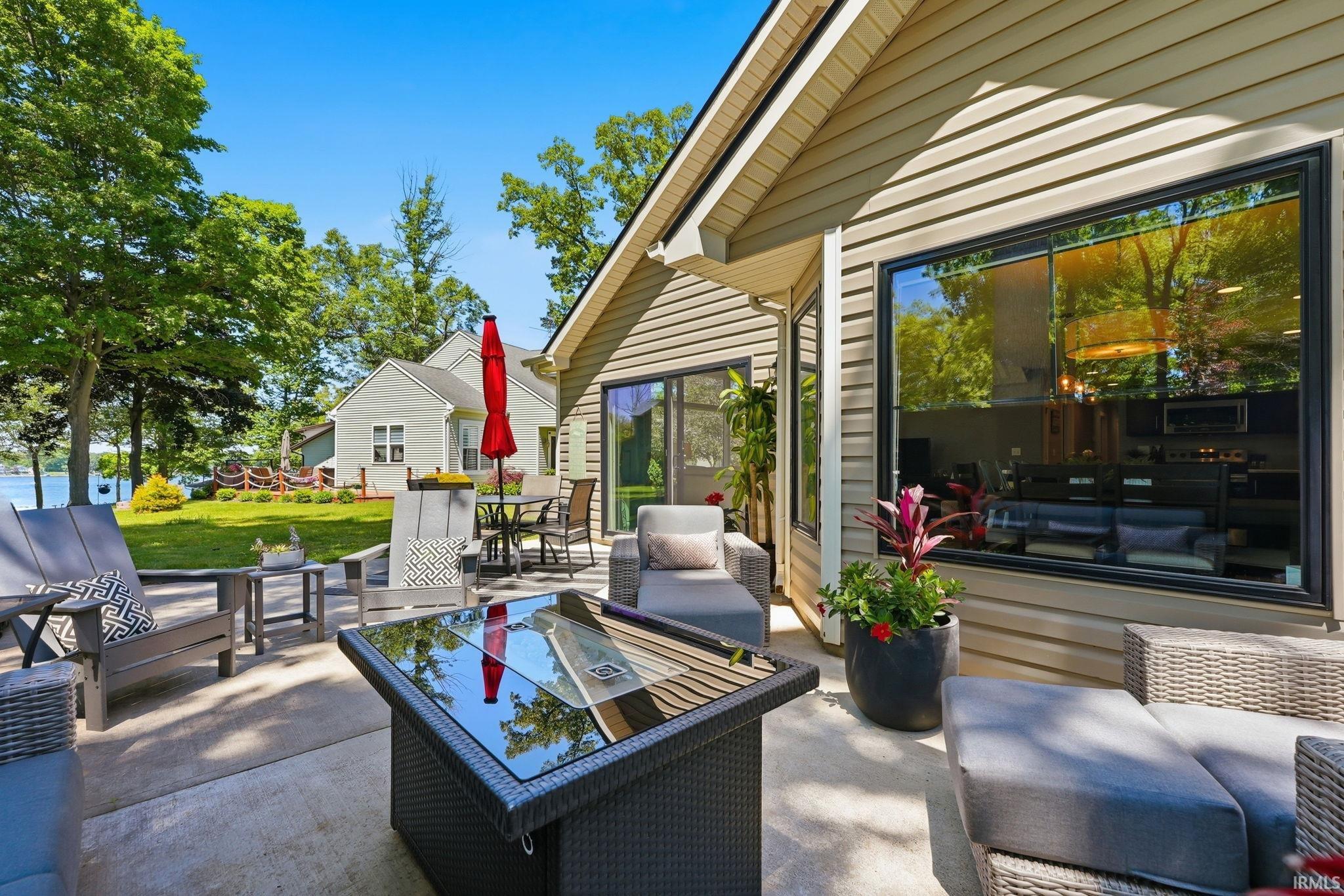 Exterior patio with concrete hardscaping, large black-framed windows, beige siding, a glass-top fire pit, and a sliding glass door