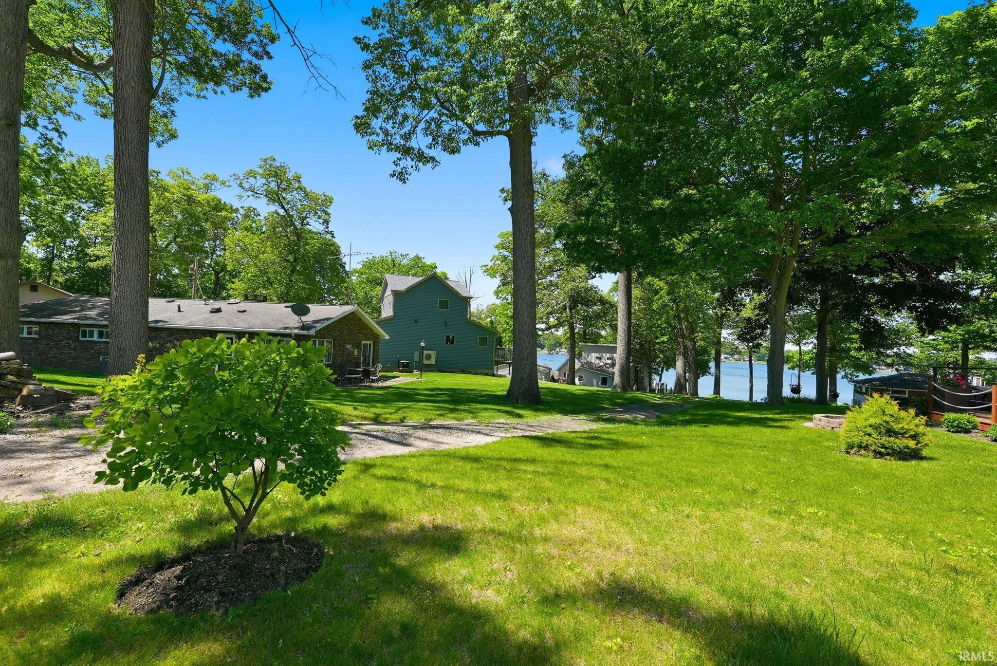 Expansive green lawn with mature trees and a partial water body visible through the foliage