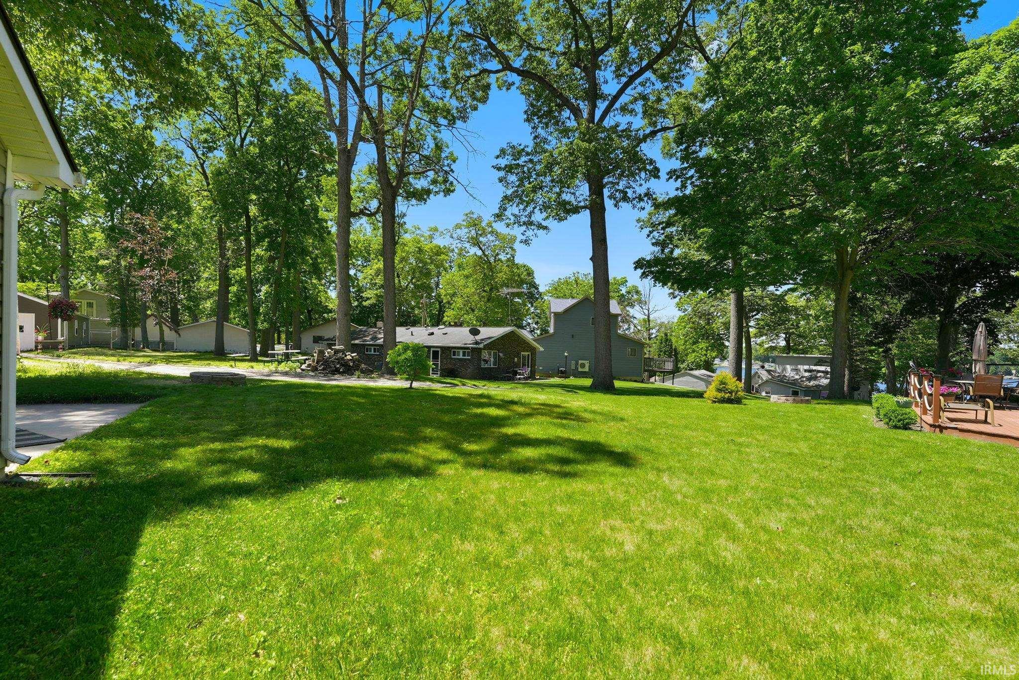 Expansive green lawn surrounded by mature trees, featuring a wooden deck with railing