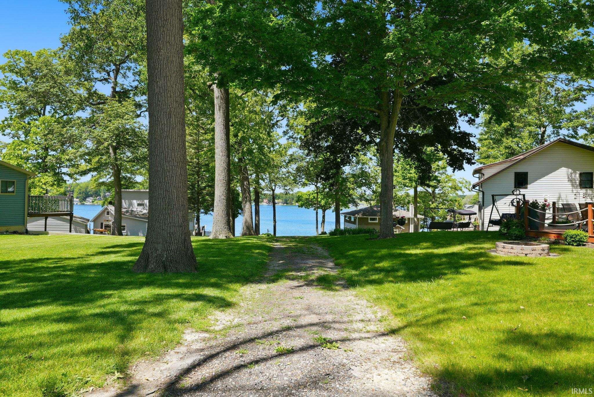 Expansive grassy yard with mature trees and a gravel path leading towards a lakefront
