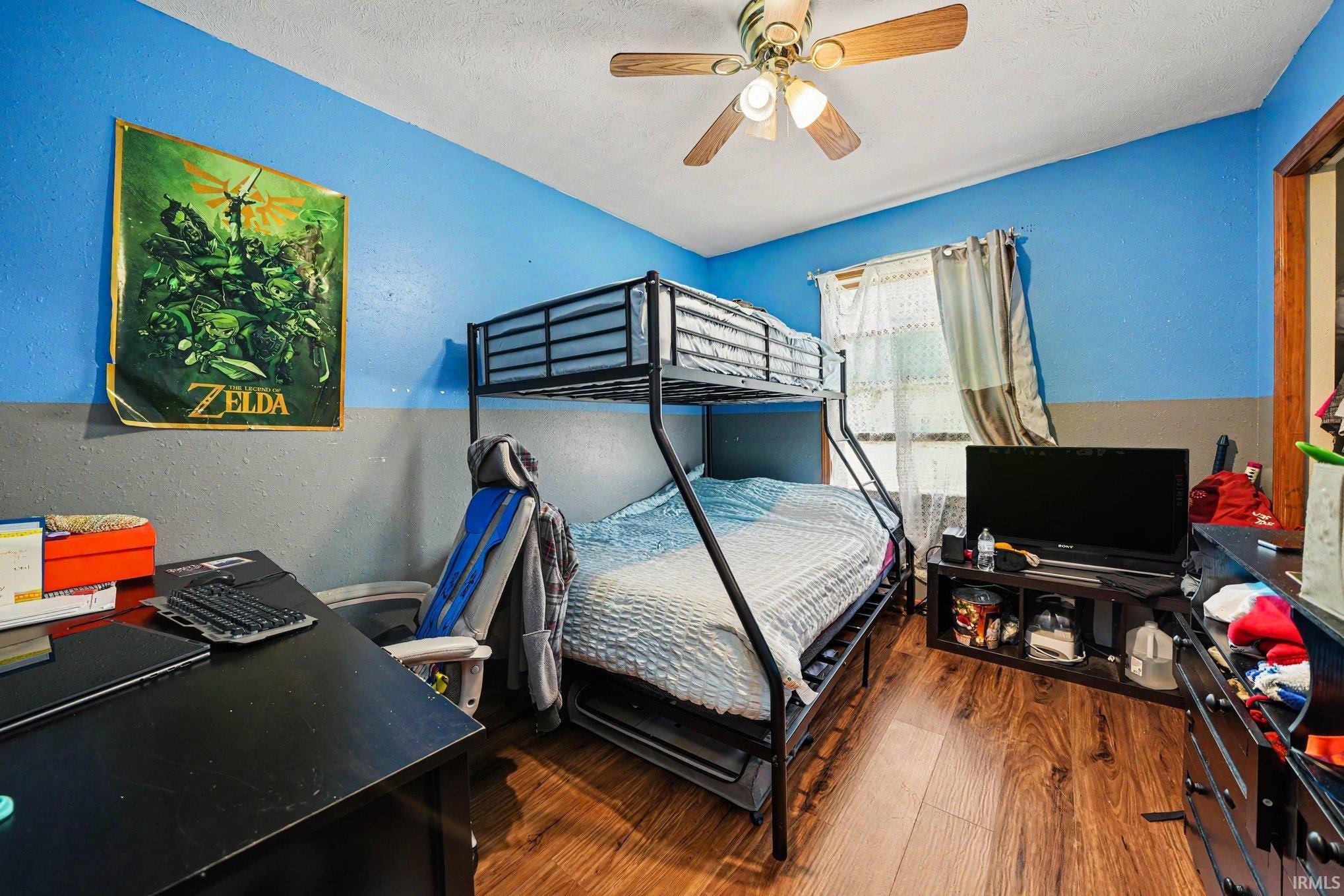 Bedroom featuring wood-finish flooring, a ceiling fan, and a window with curtains