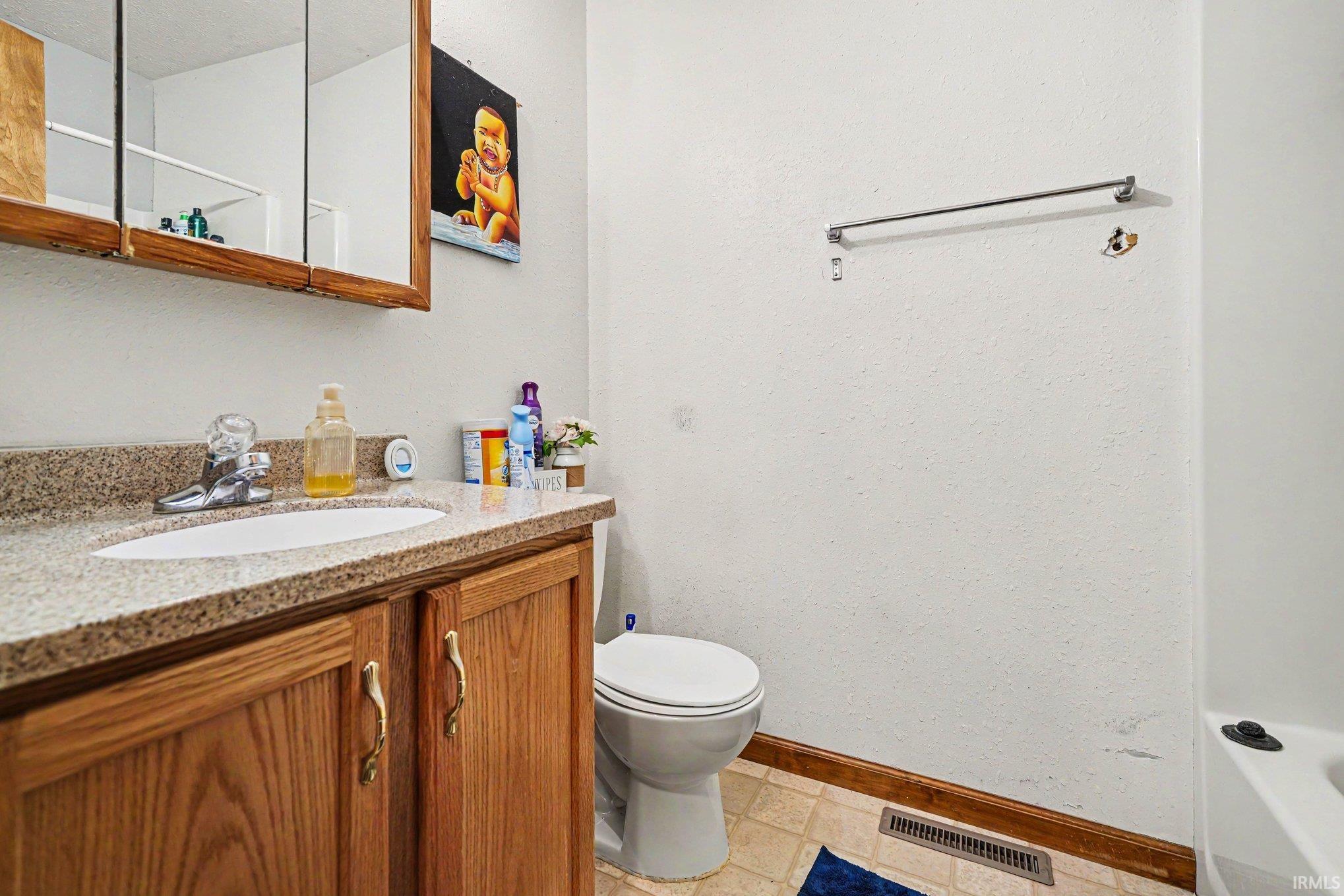 Bathroom featuring a wood-finish vanity with a built-in sink, solid surface countertop, and mirrored medicine cabinet