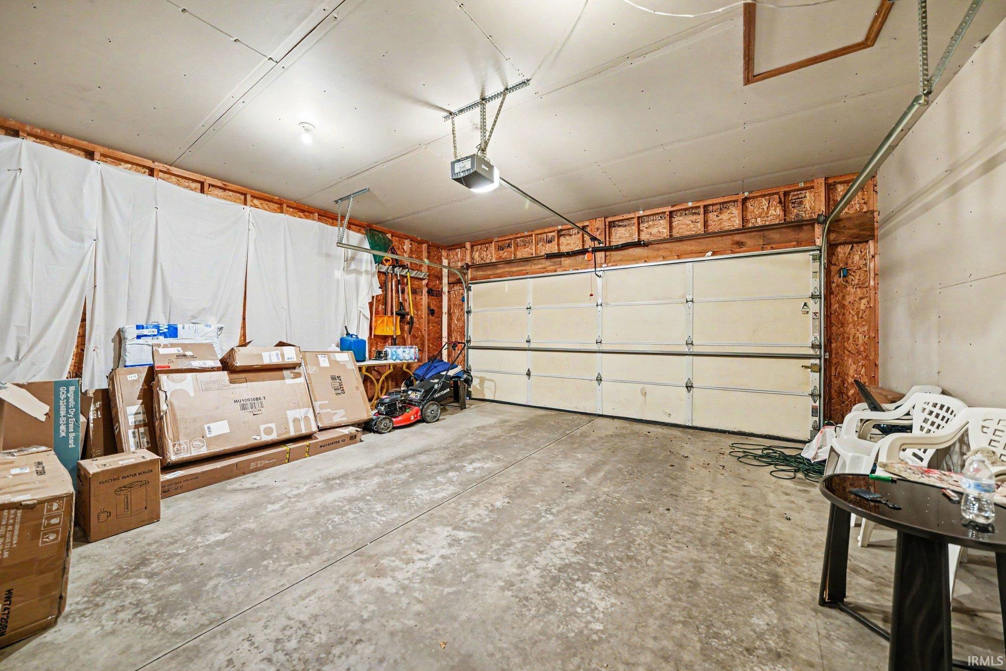 Attached garage featuring a concrete floor, exposed wood framing, and an overhead garage door with an automatic opener