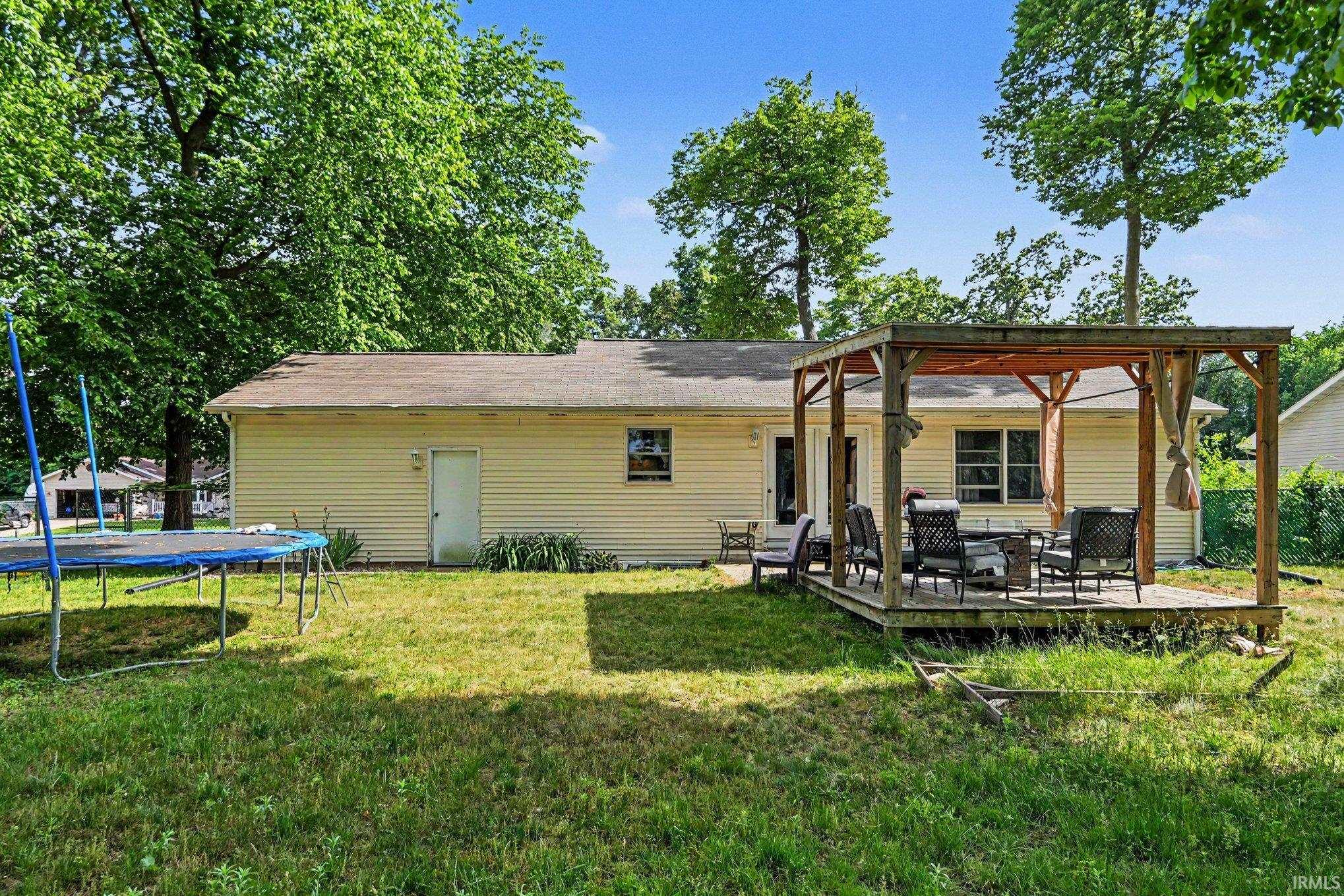 Expansive backyard featuring a wood deck with a pergola, mature trees, and a beige vinyl siding exterior