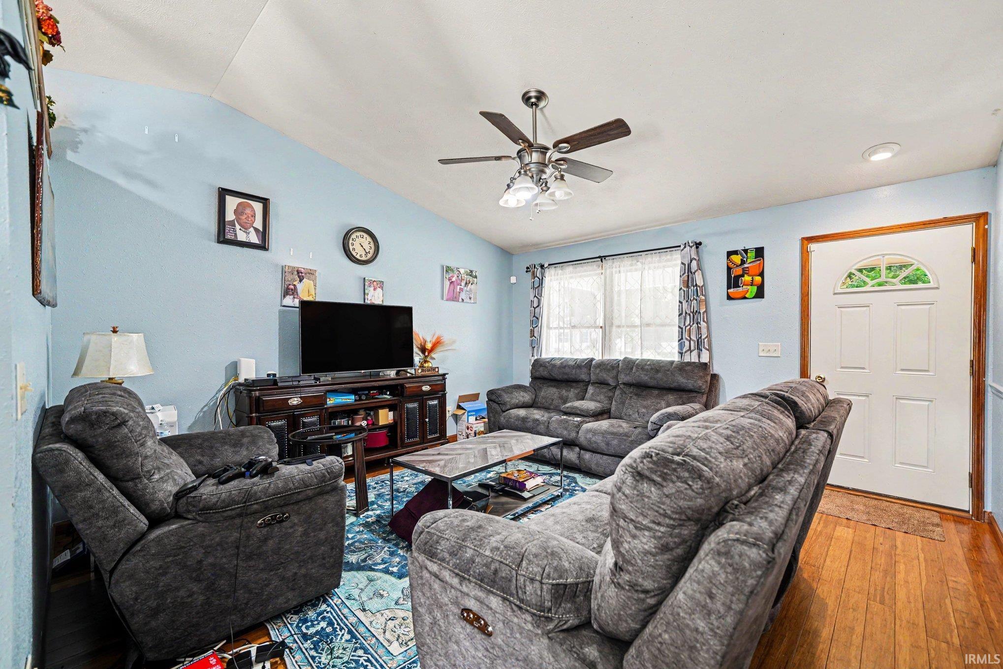 Living area featuring wood-finish flooring, vaulted ceiling, and light blue walls